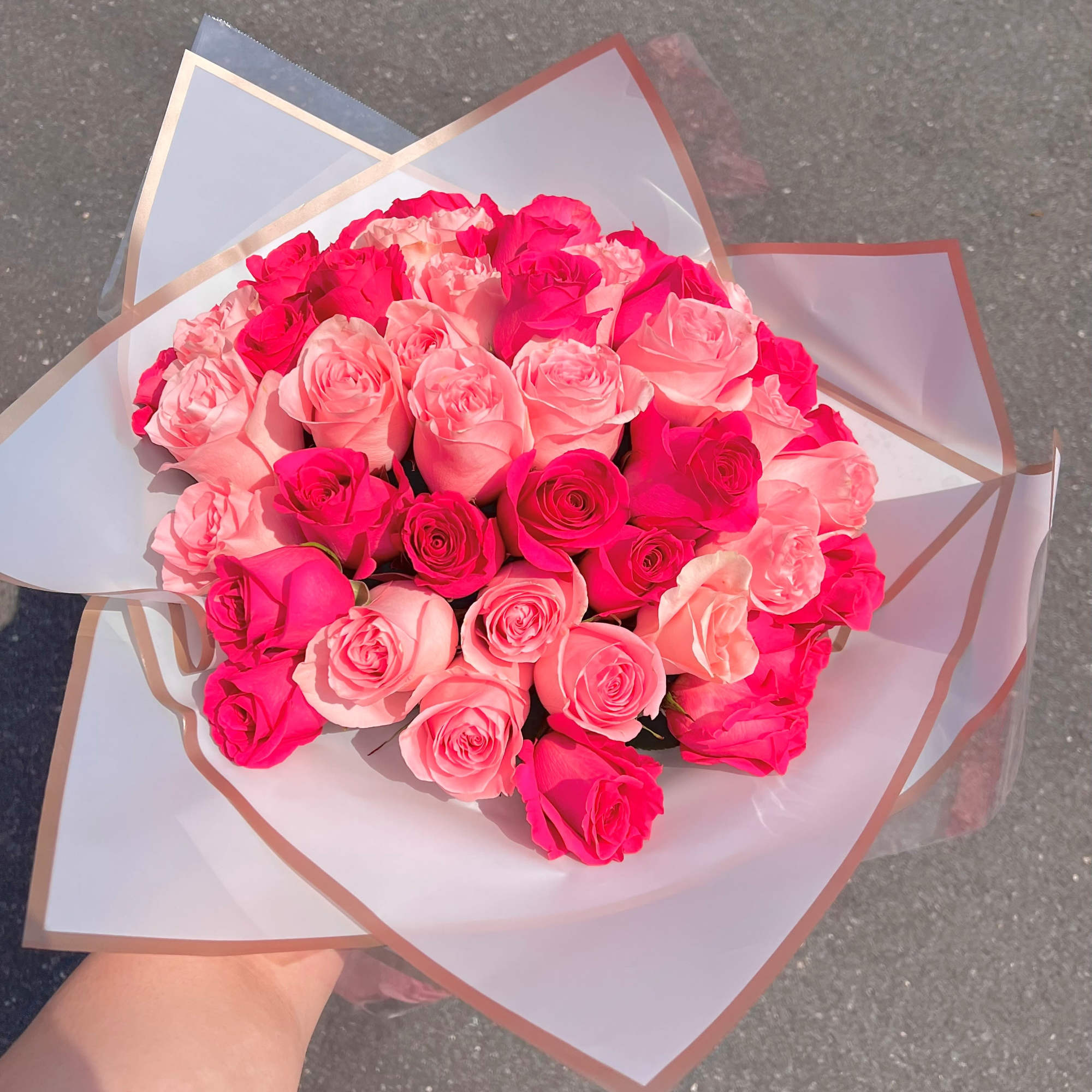 Hand-tied bouquet of hot pink and light pink roses wrapped in white paper with gold trim
