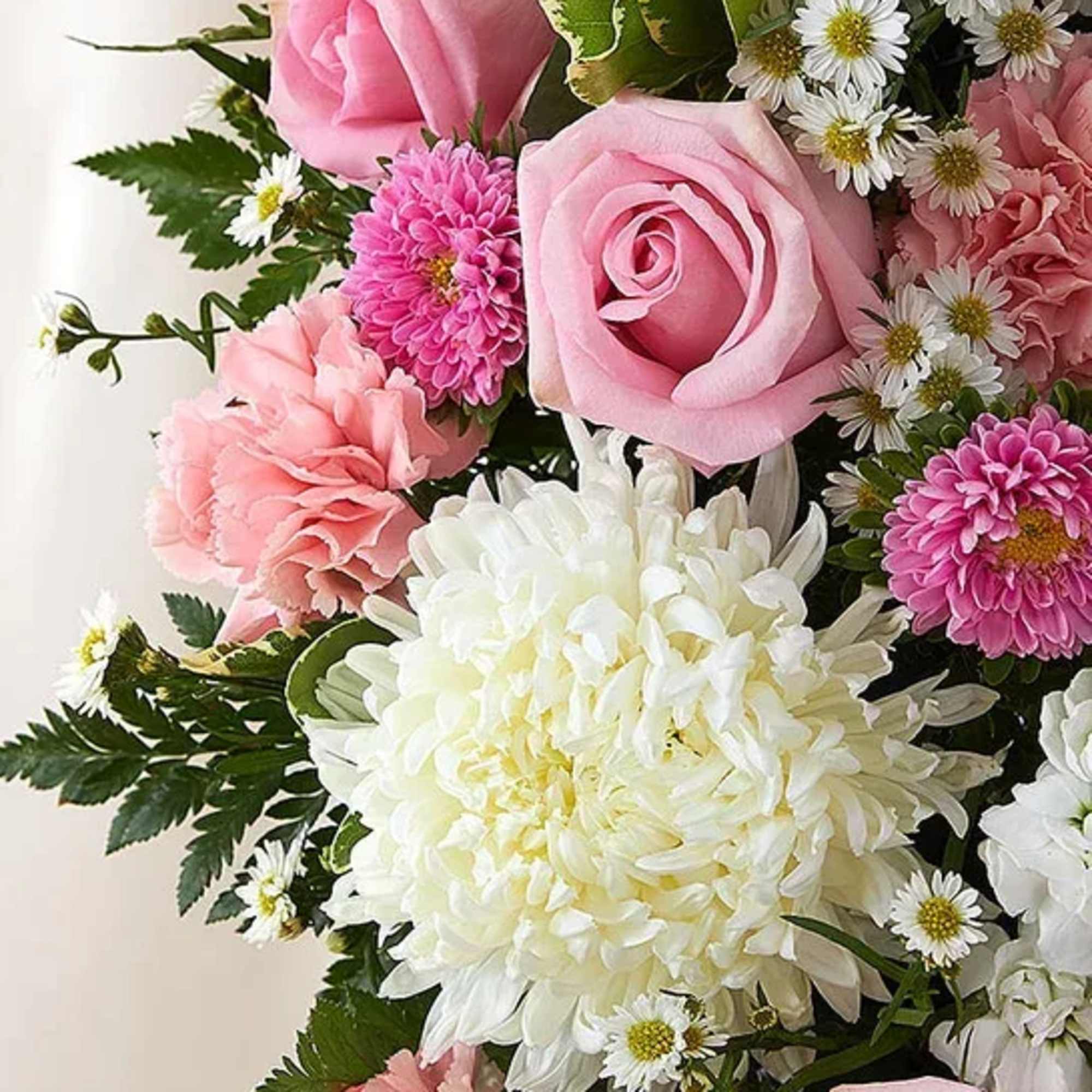 Close-up of a pastel arrangement with pink roses, pink carnations, white mums and small white daisies.