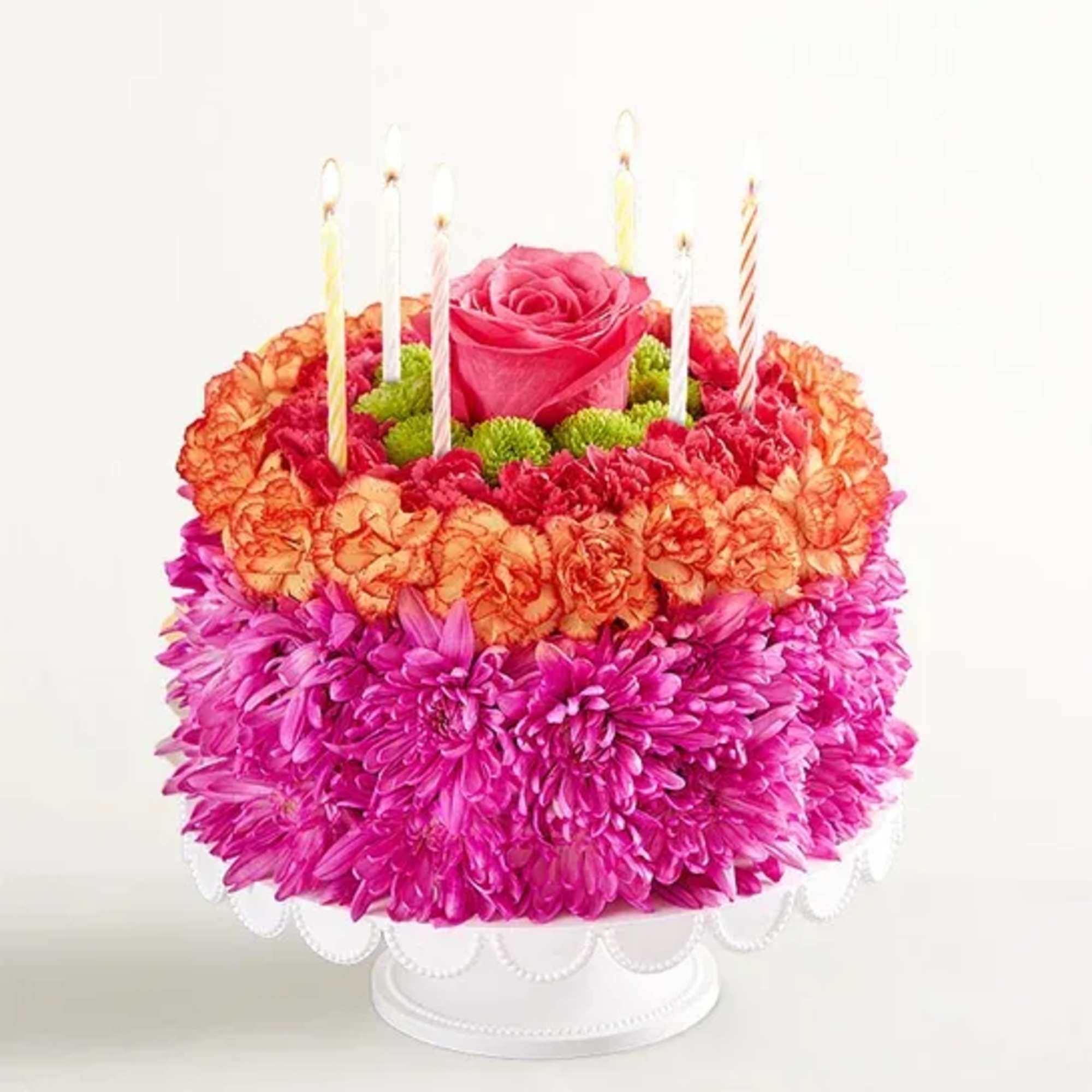 Flower-covered cake with candles and a pink rose on top