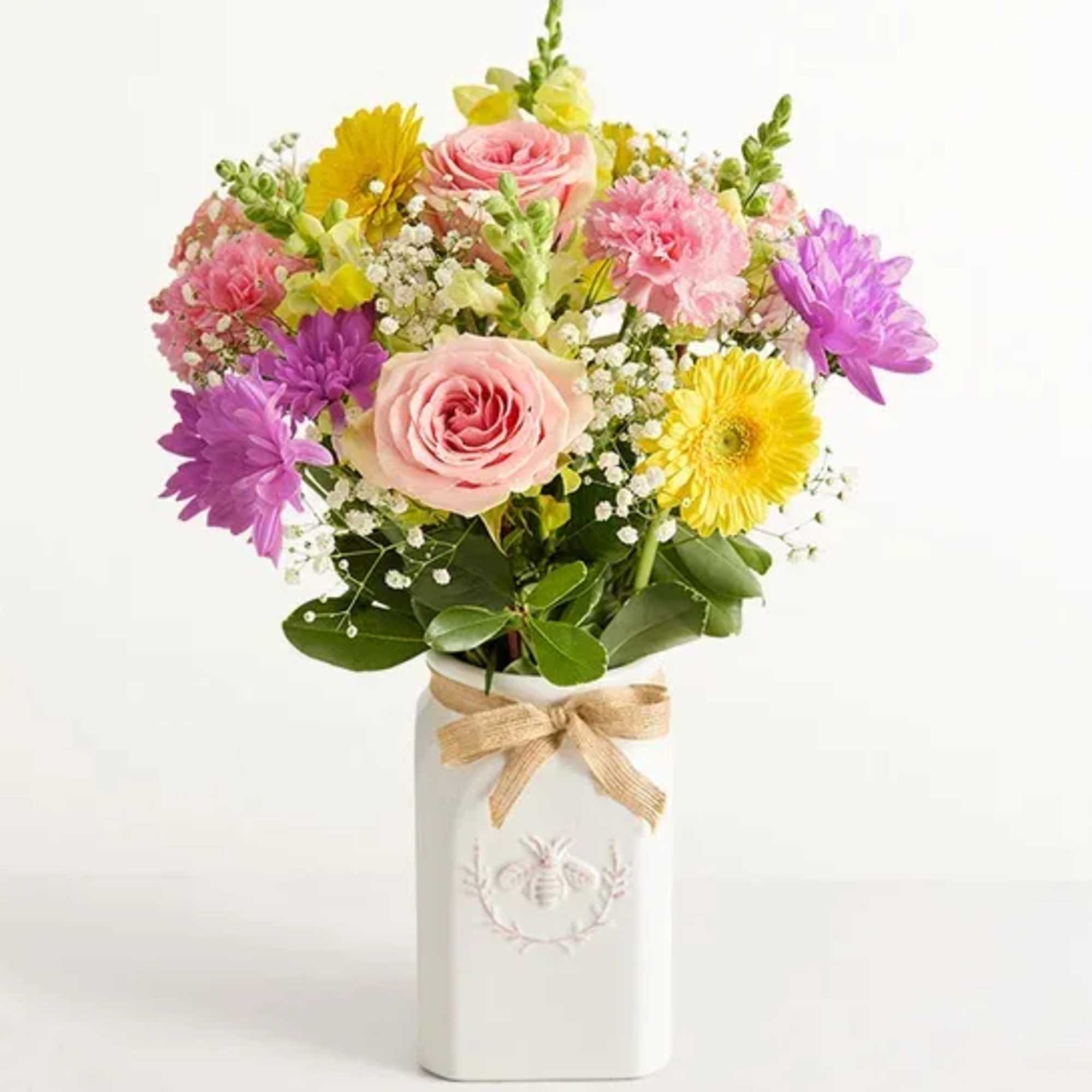 Mixed bouquet of pink, yellow, and purple flowers in a white vase