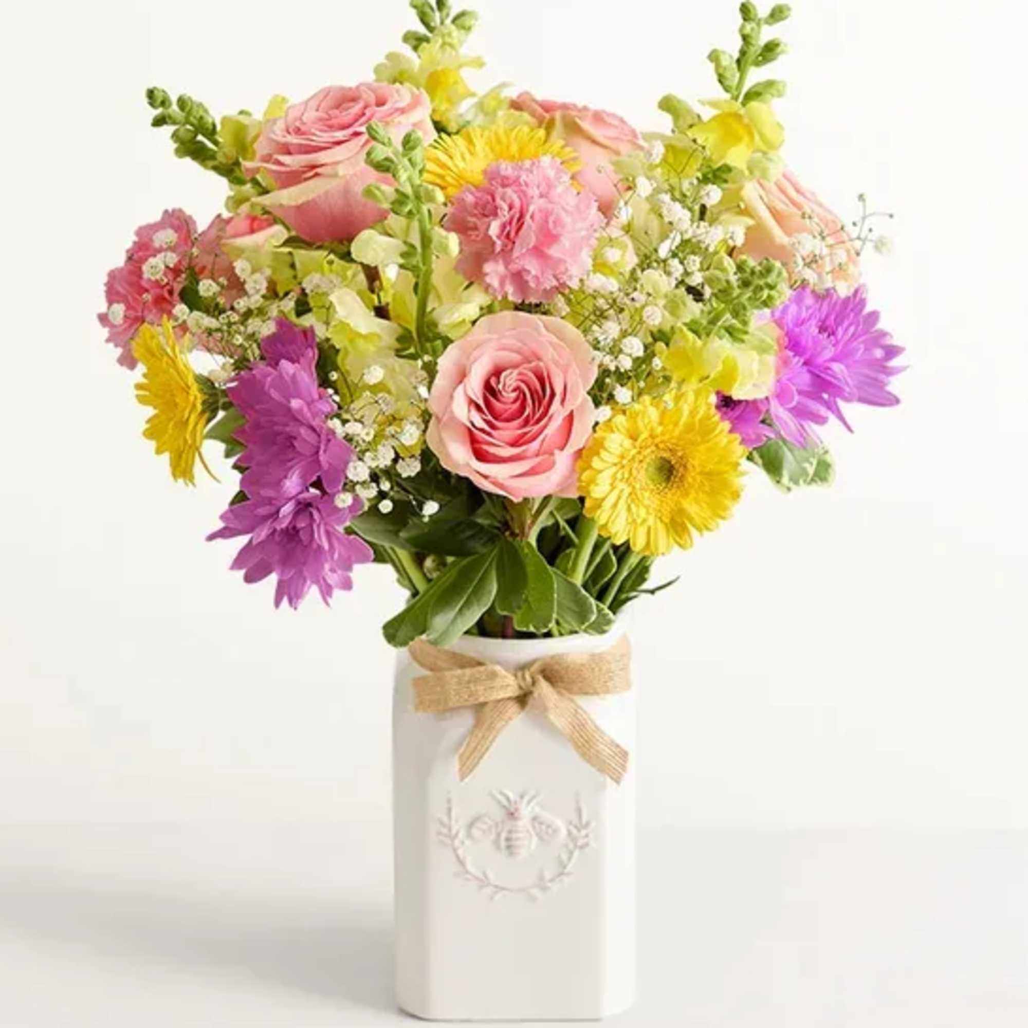 Mixed bouquet of pink, yellow, and purple flowers in a white vase