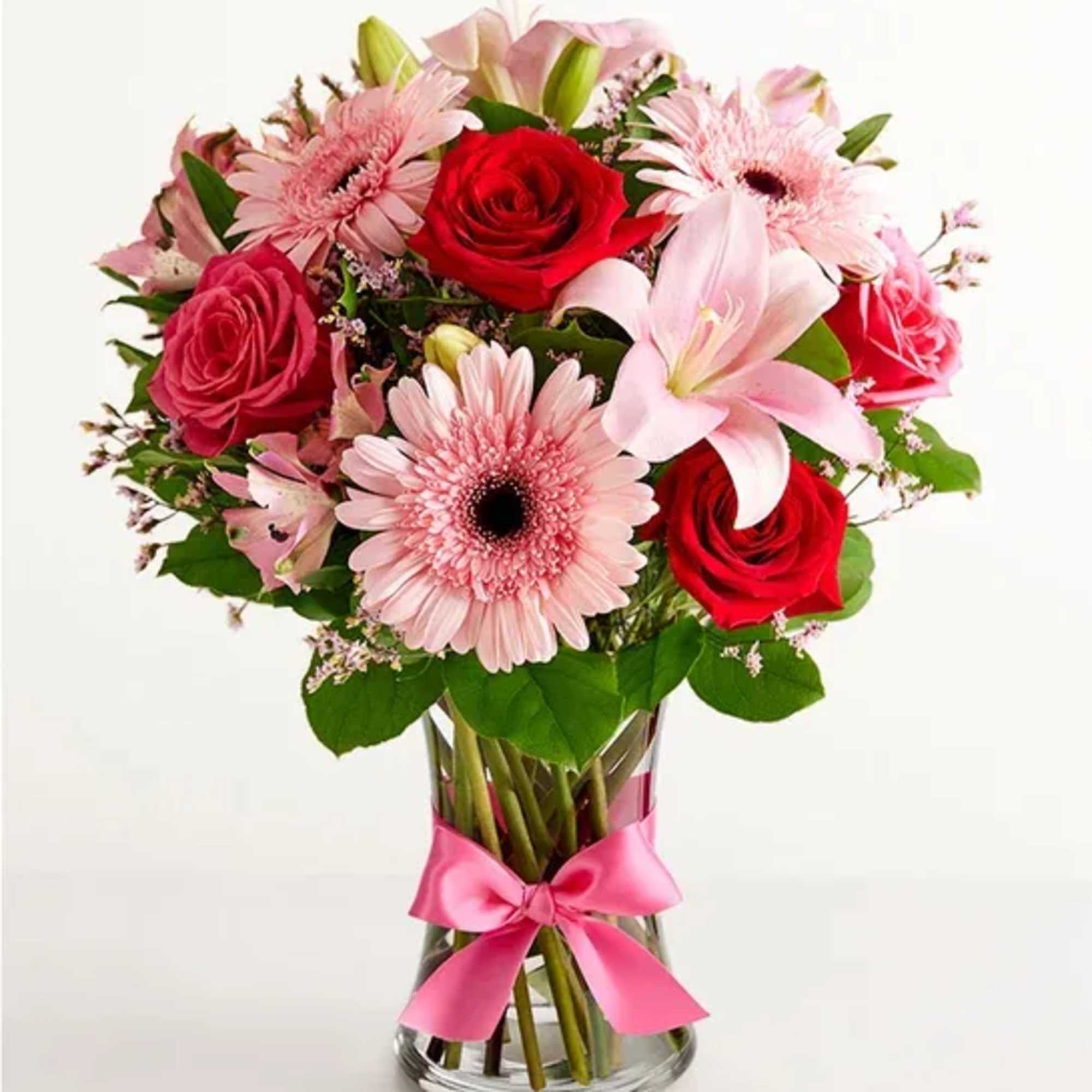 Pink and red bouquet of roses, gerbera daisies, and lilies in a glass vase