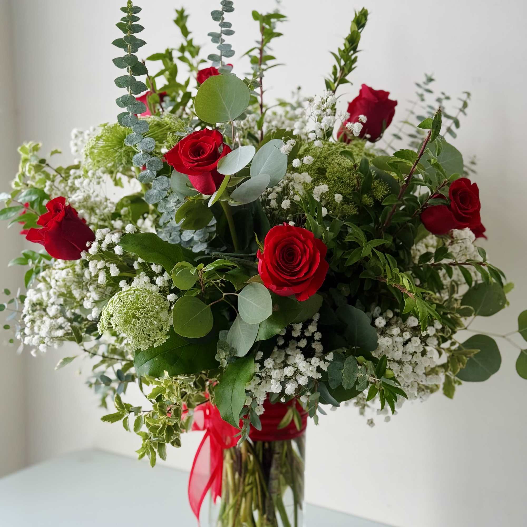 Arrangement of red roses and white filler flowers in a tall glass vase with a red ribbon.
