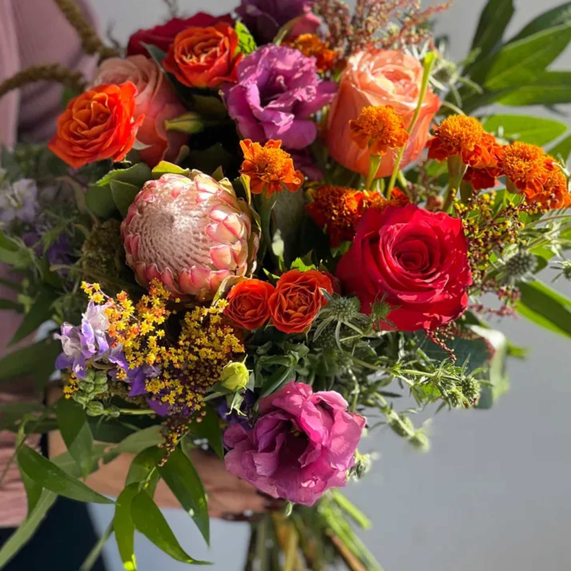 Handheld bouquet with roses, protea, and orange accent flowers