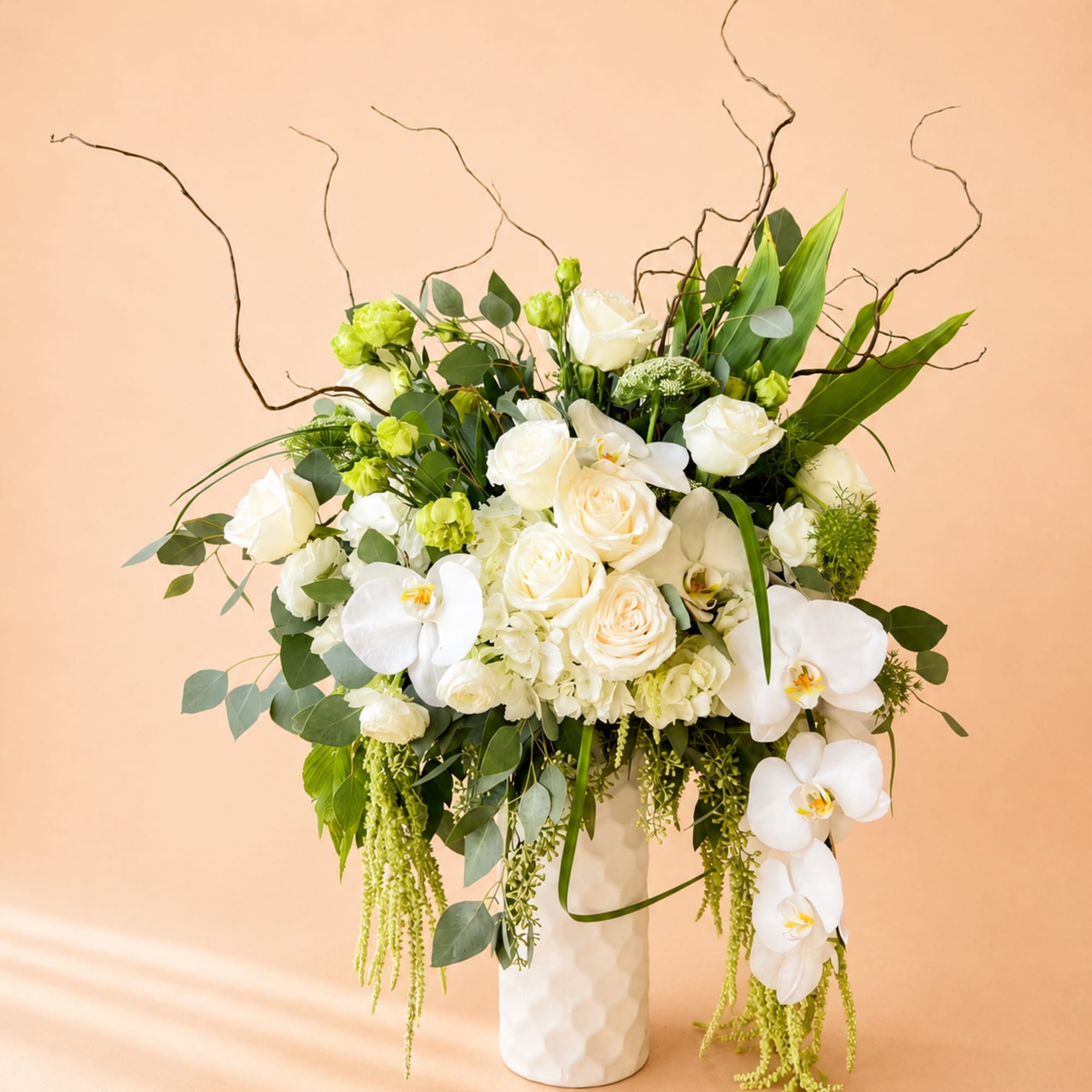 White roses and orchids in a tall white vase with greenery
