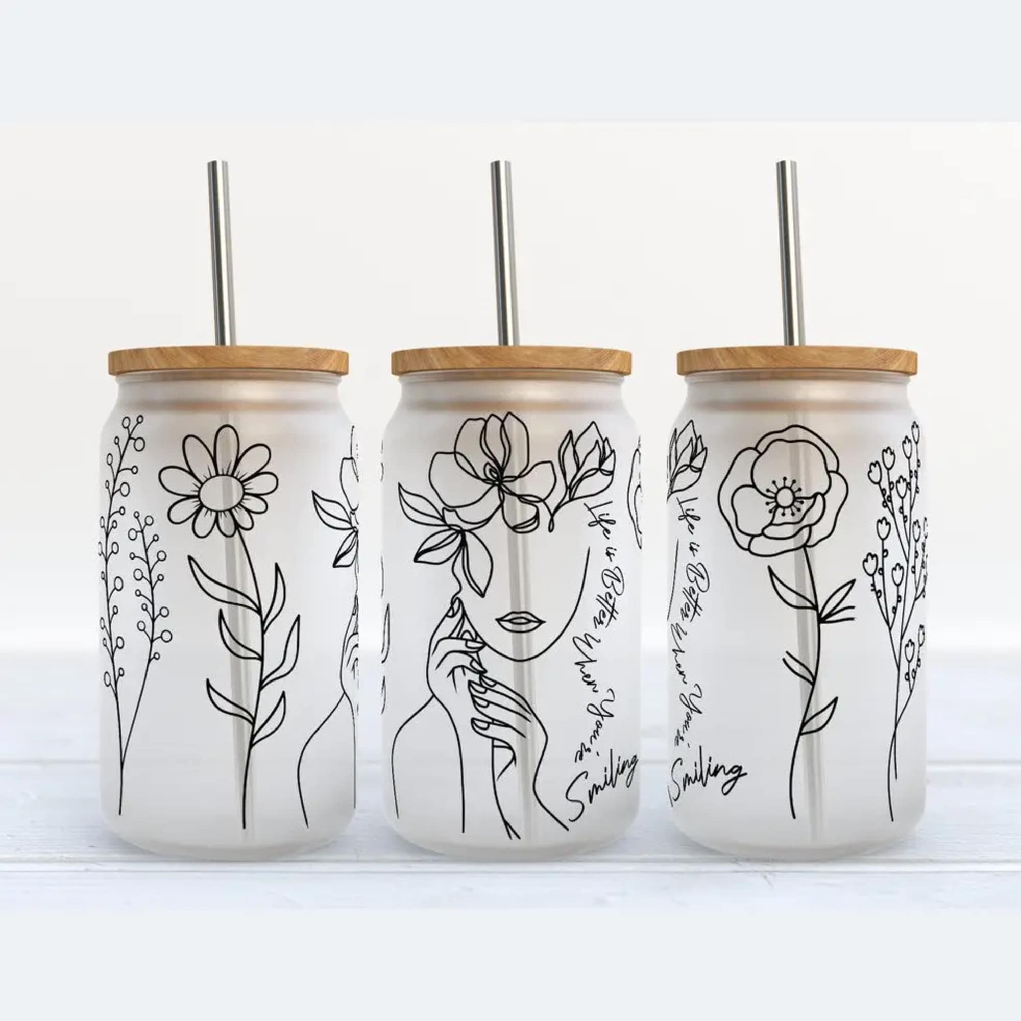 Three frosted glass tumblers with floral line art and metal straws