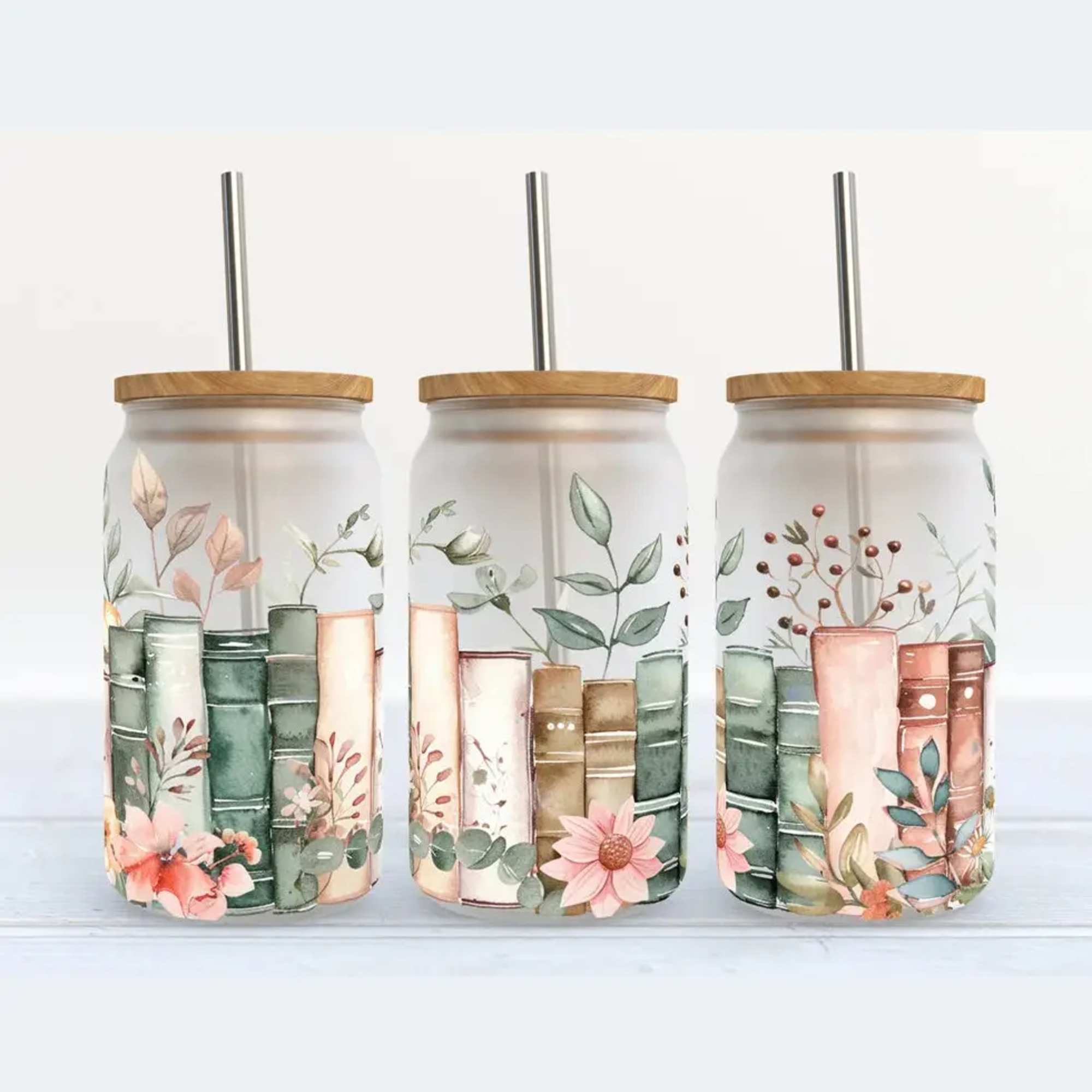 Three floral-printed glass tumblers with wooden lids and metal straws