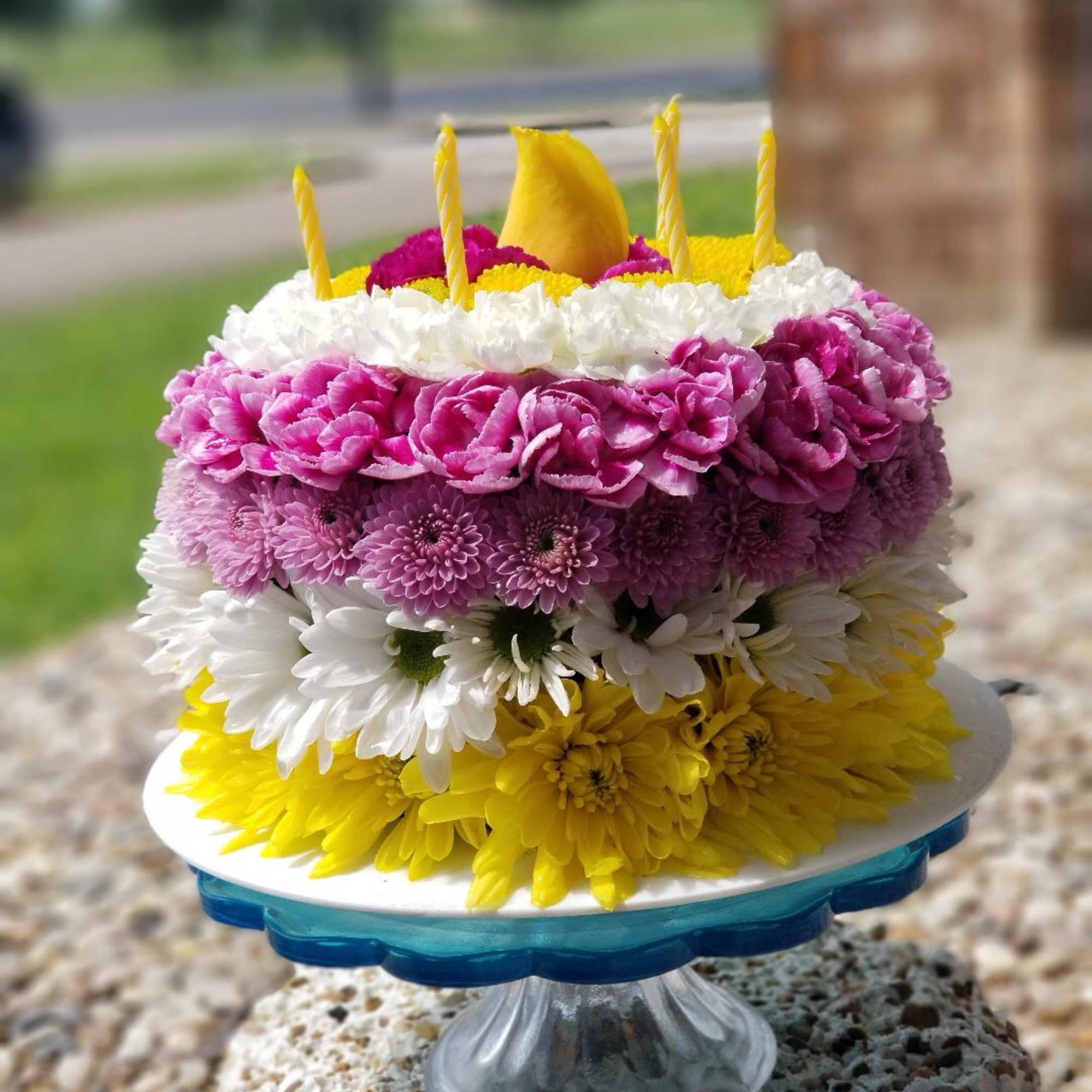 Tiered floral cake with yellow, pink, white, and purple flowers and candles