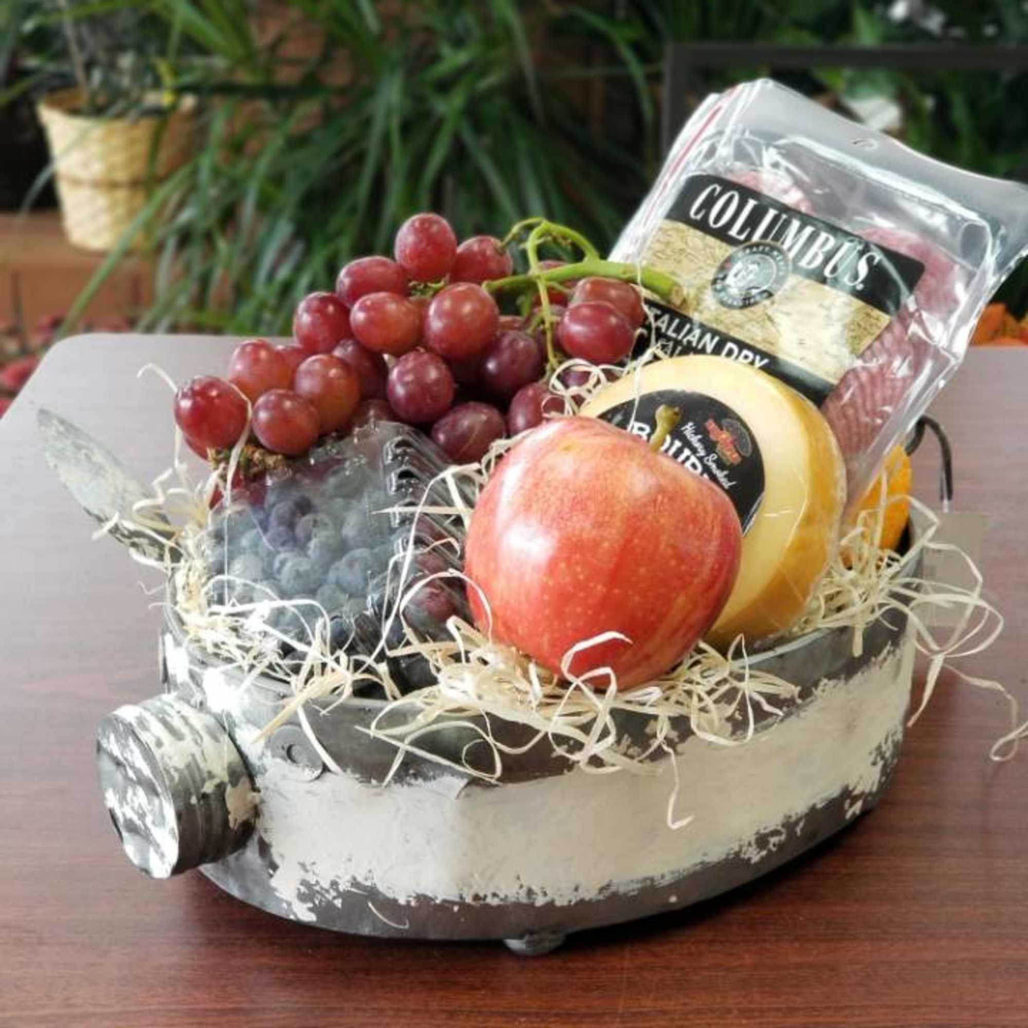 Fruit gift basket with grapes, an apple, and packaged cheese in a decorative tray