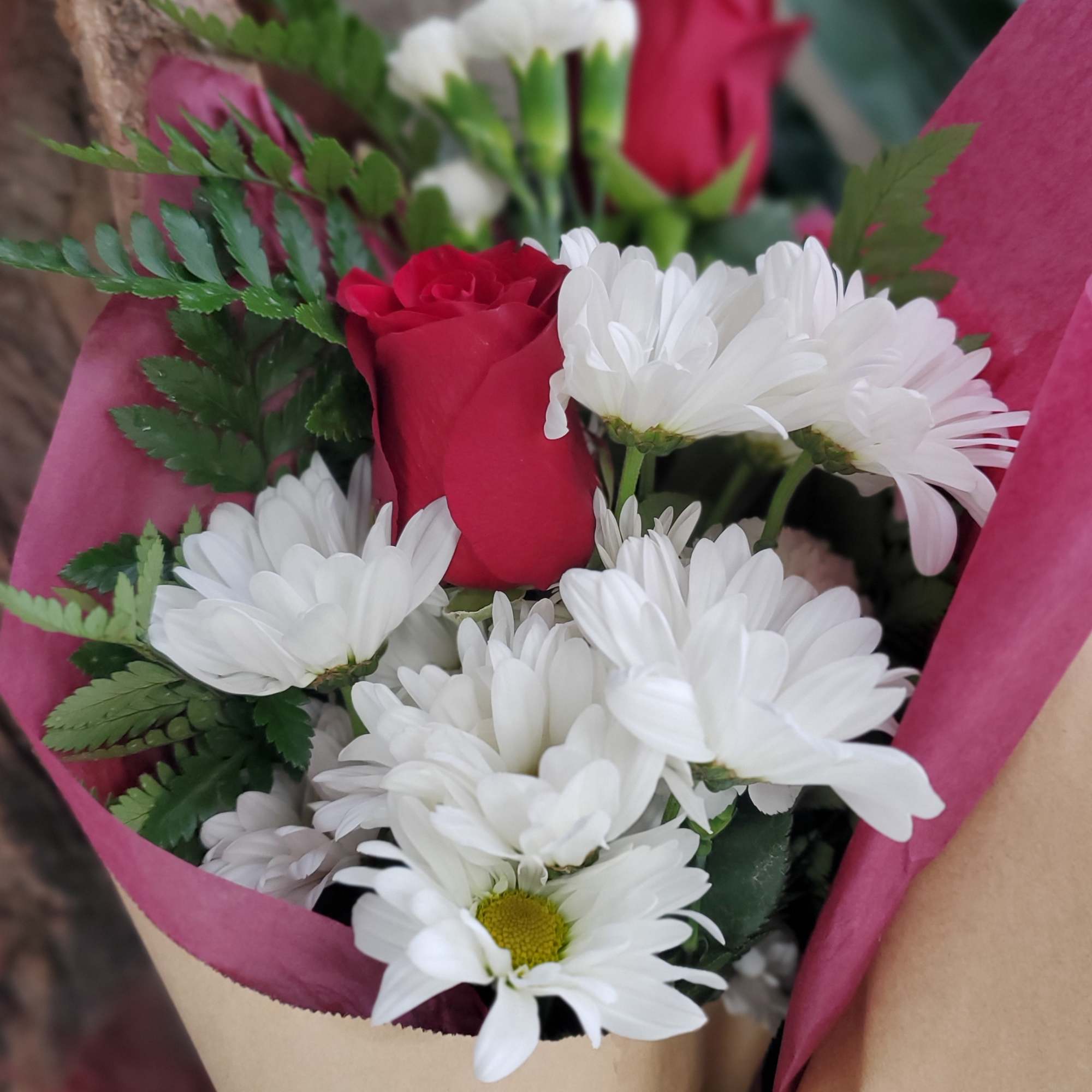 Bouquet of red roses and white daisies wrapped in pink paper