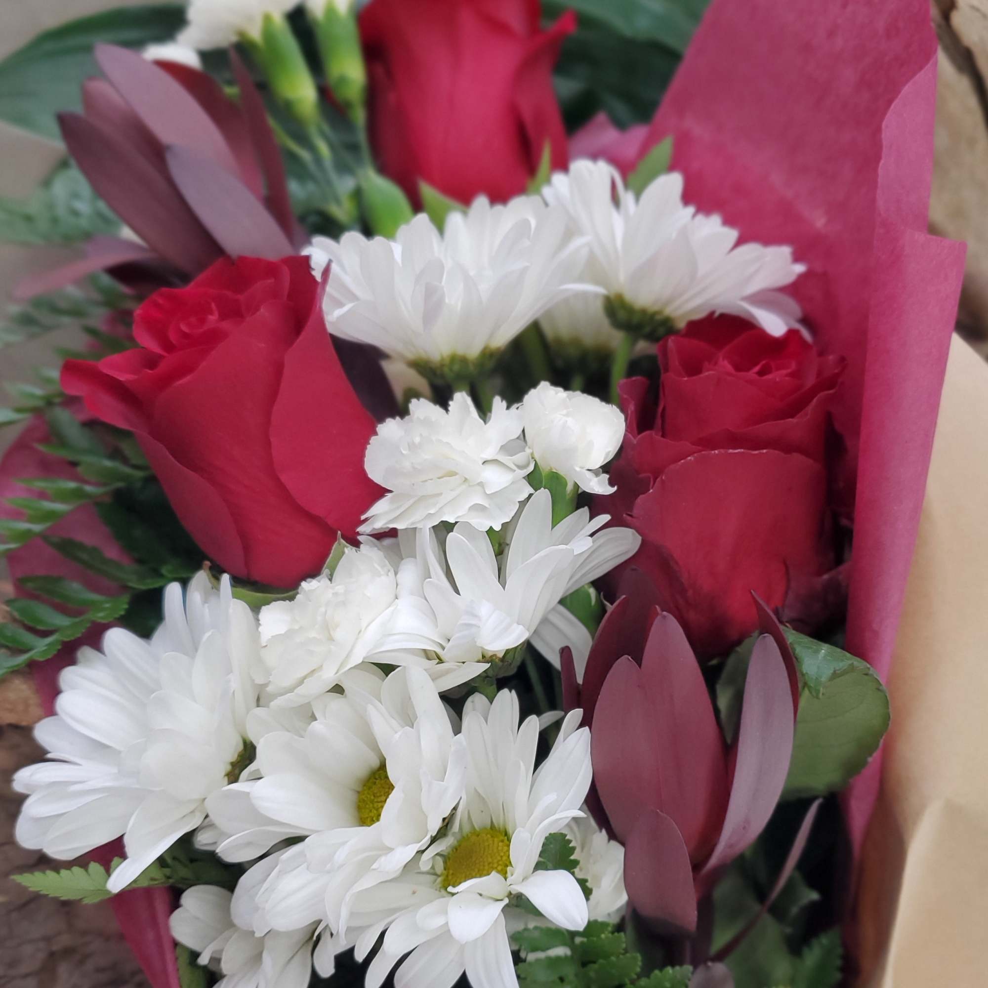 Bouquet of red roses and white daisies wrapped in pink paper
