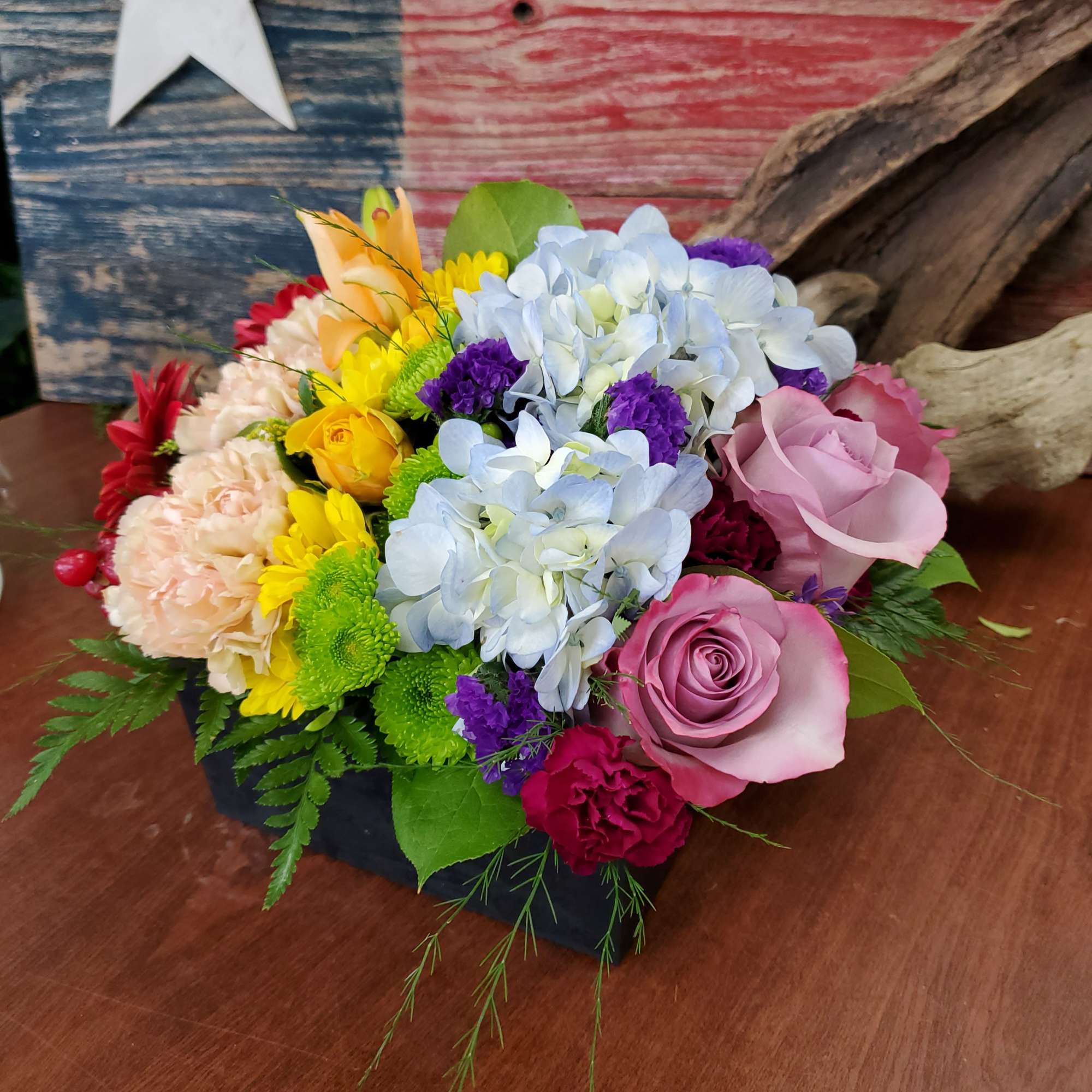 Colorful mixed flower arrangement in a black container with roses and hydrangeas