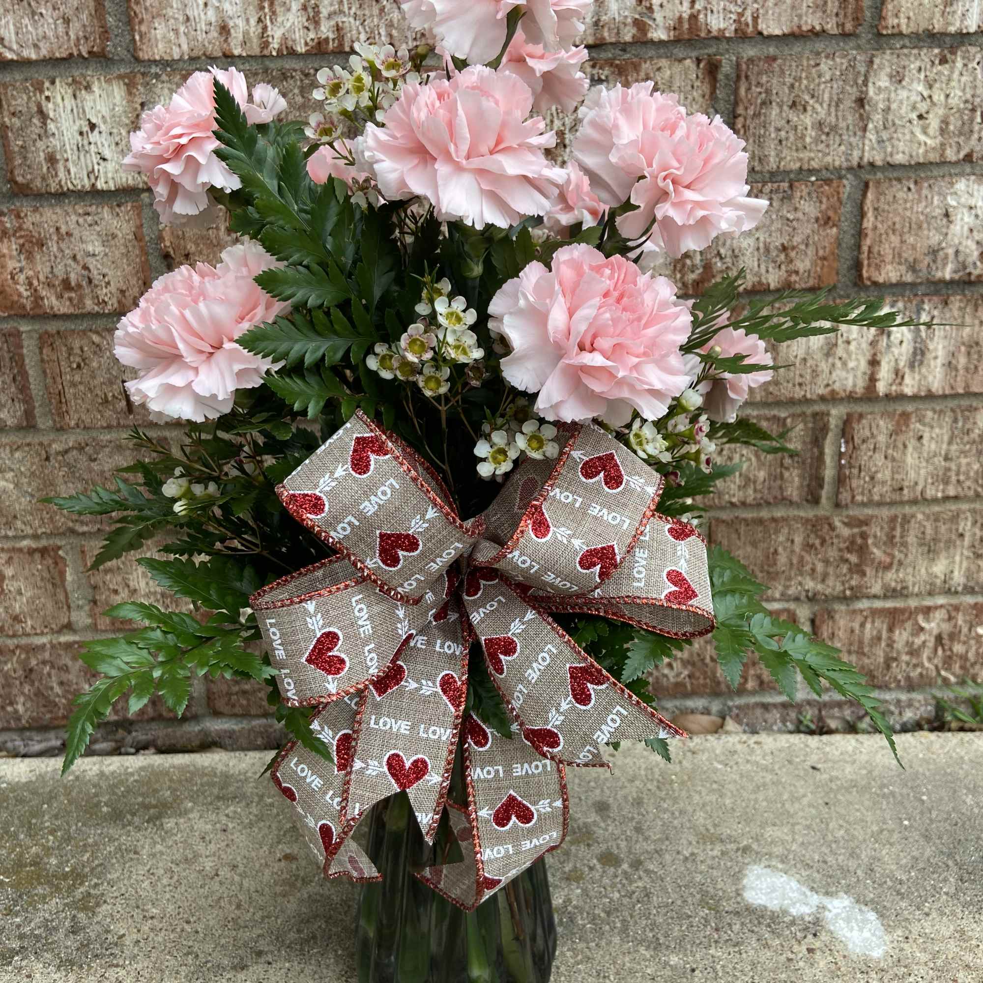 Pink carnations in a glass vase with a heart-patterned ribbon