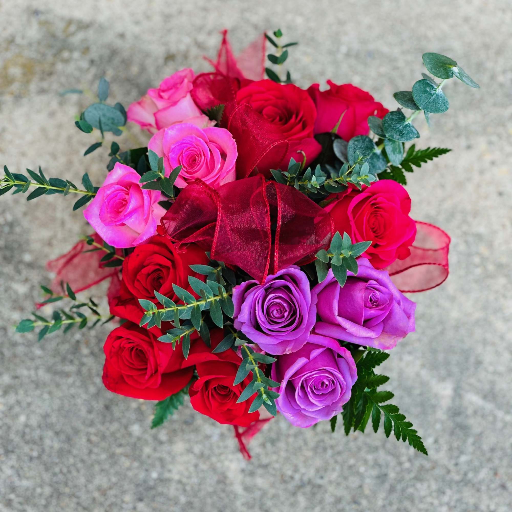 Bouquet of red, pink, and purple roses with a red ribbon