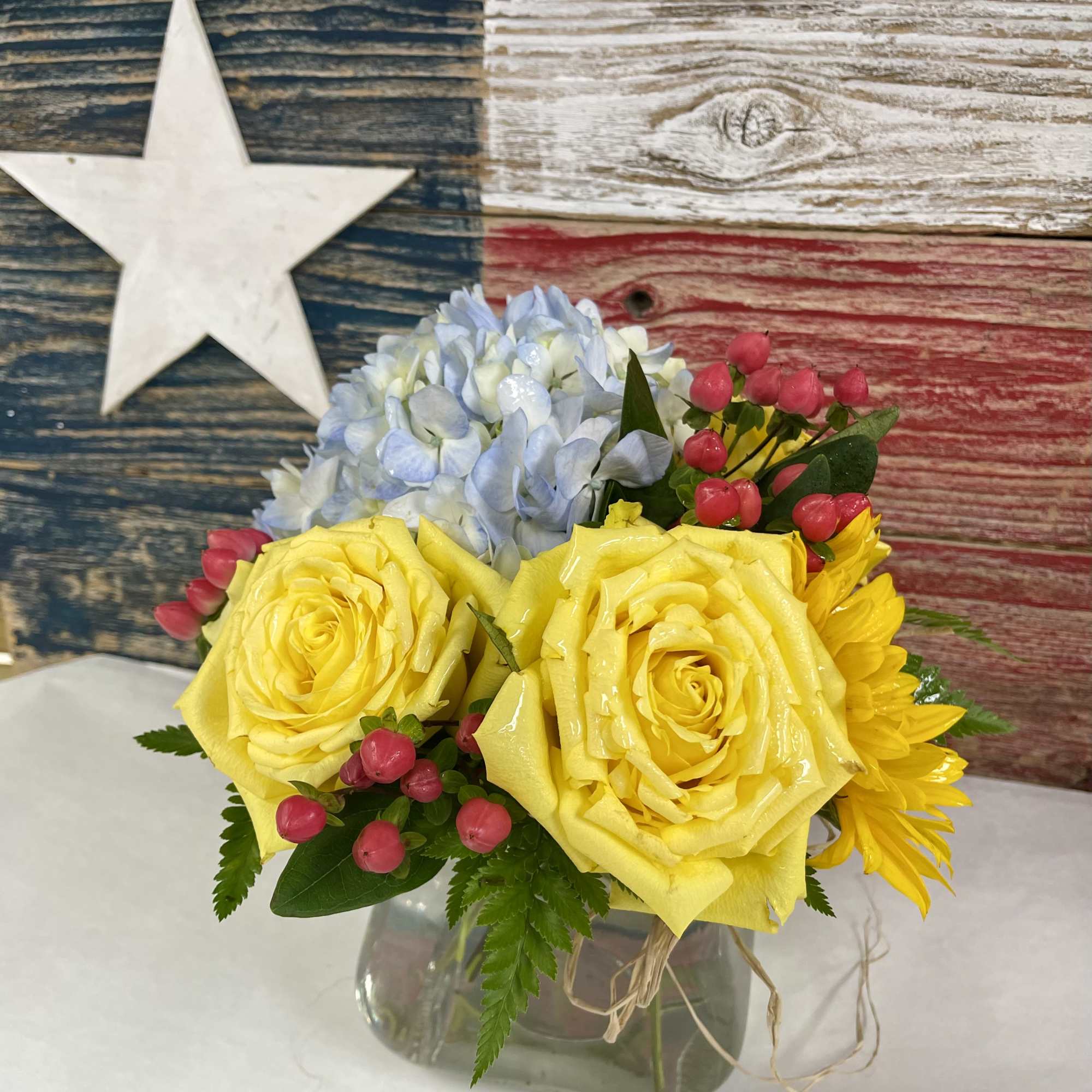 Yellow roses and blue hydrangea in a glass vase with pink berries