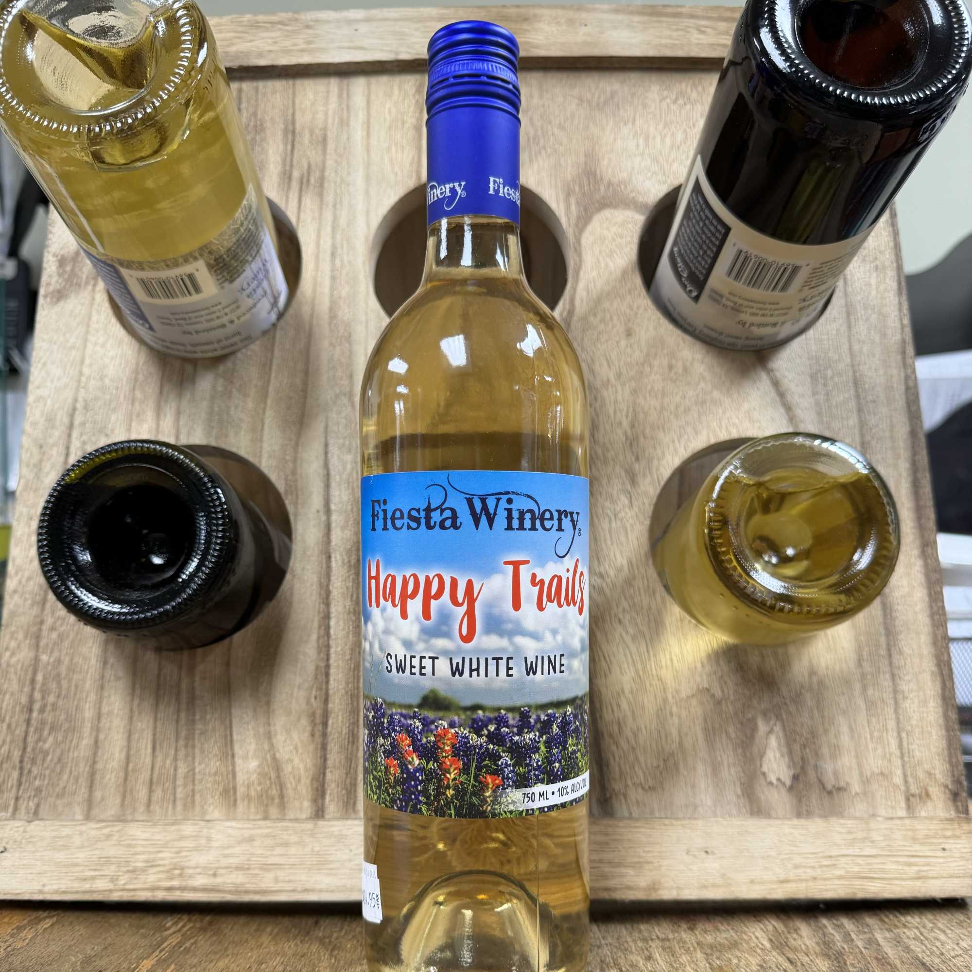 Five wine bottles arranged in a wooden carrier, one labeled Fiesta Winery Happy Trails