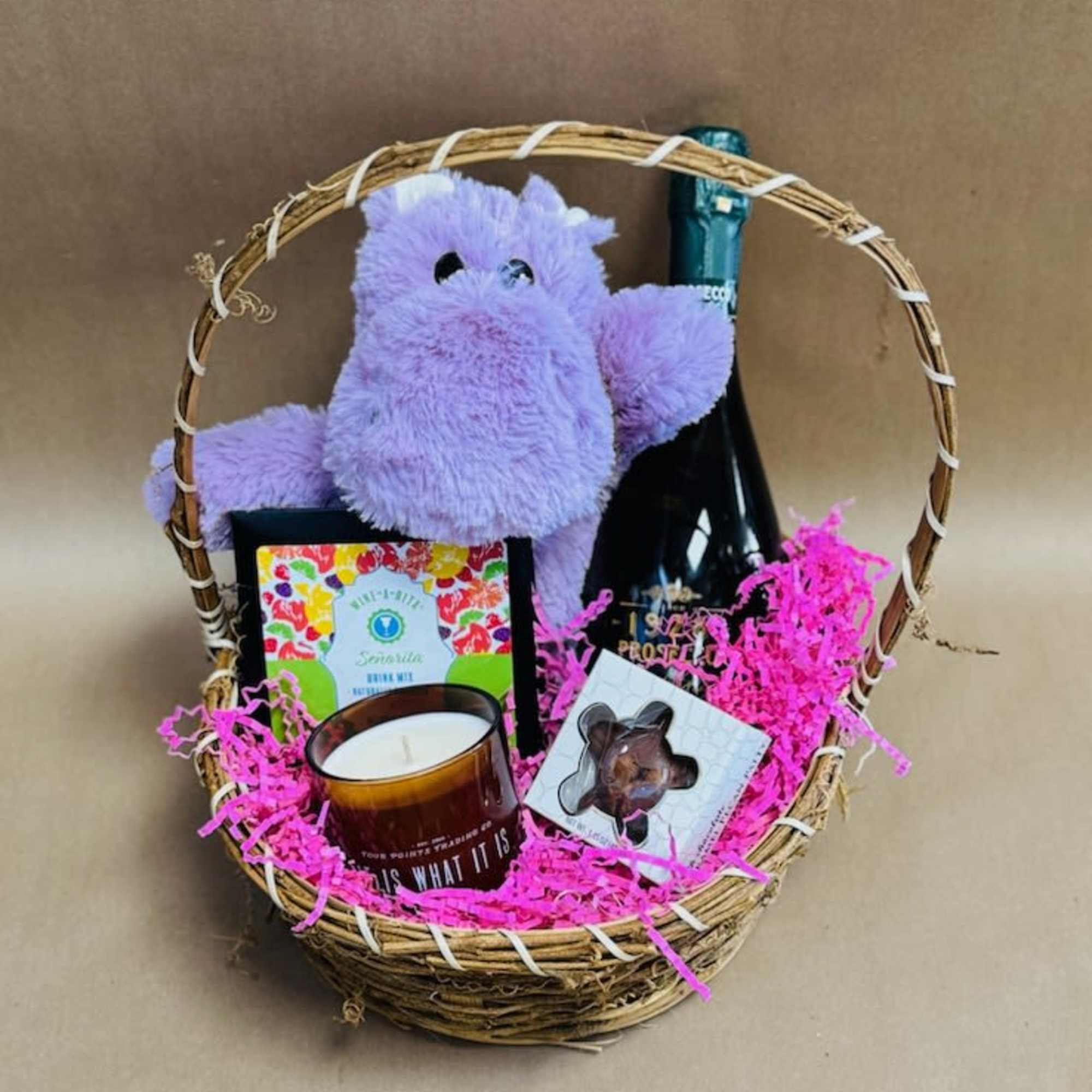 Gift basket with a plush purple hippo, candle, chocolate, and a bottle
