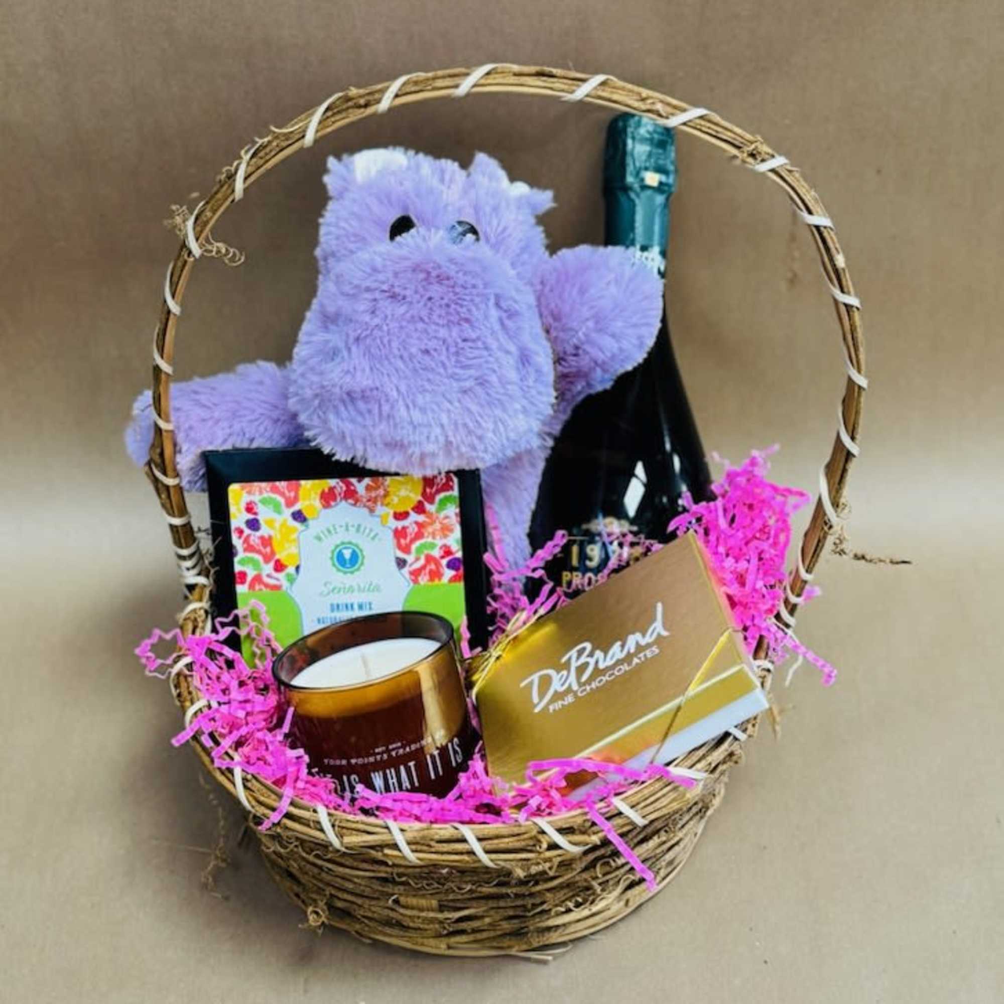 Gift basket with a plush purple hippo, wine bottle, candle, and chocolates
