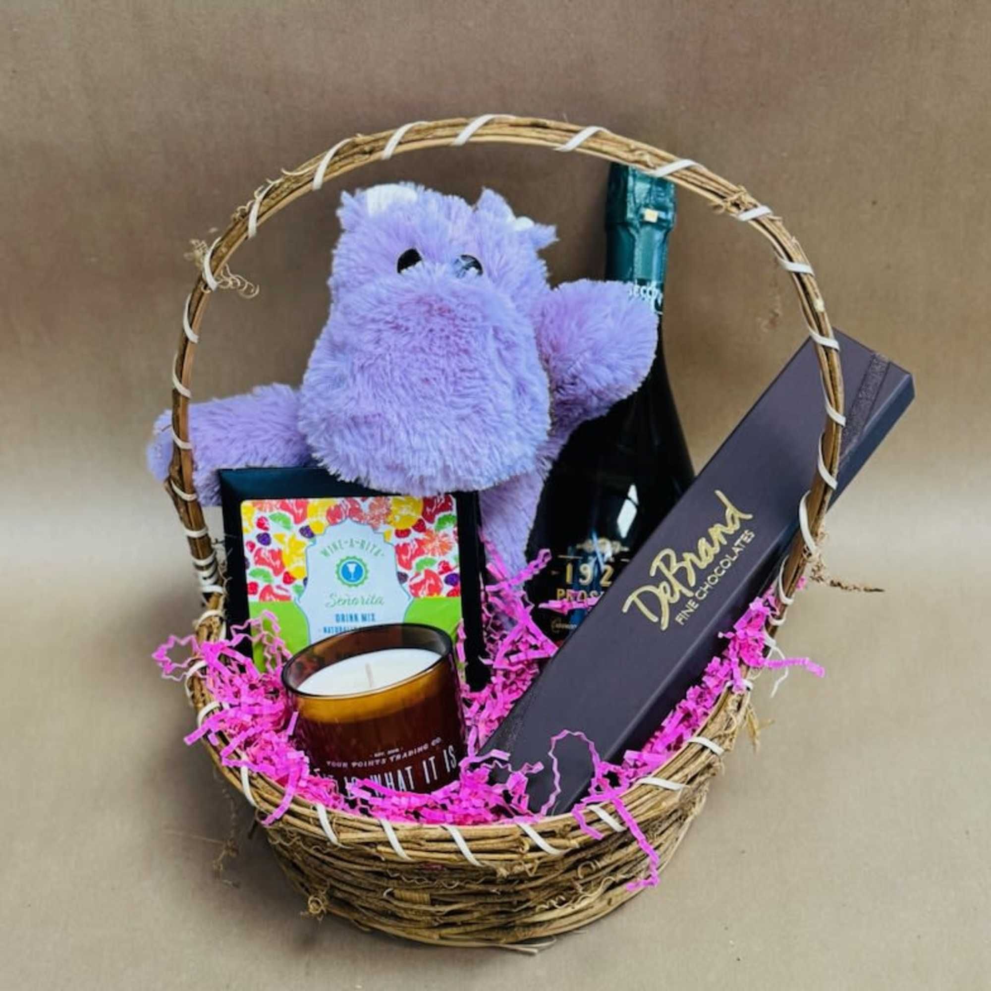 Gift basket with a purple plush toy, candle, chocolates, and a bottle