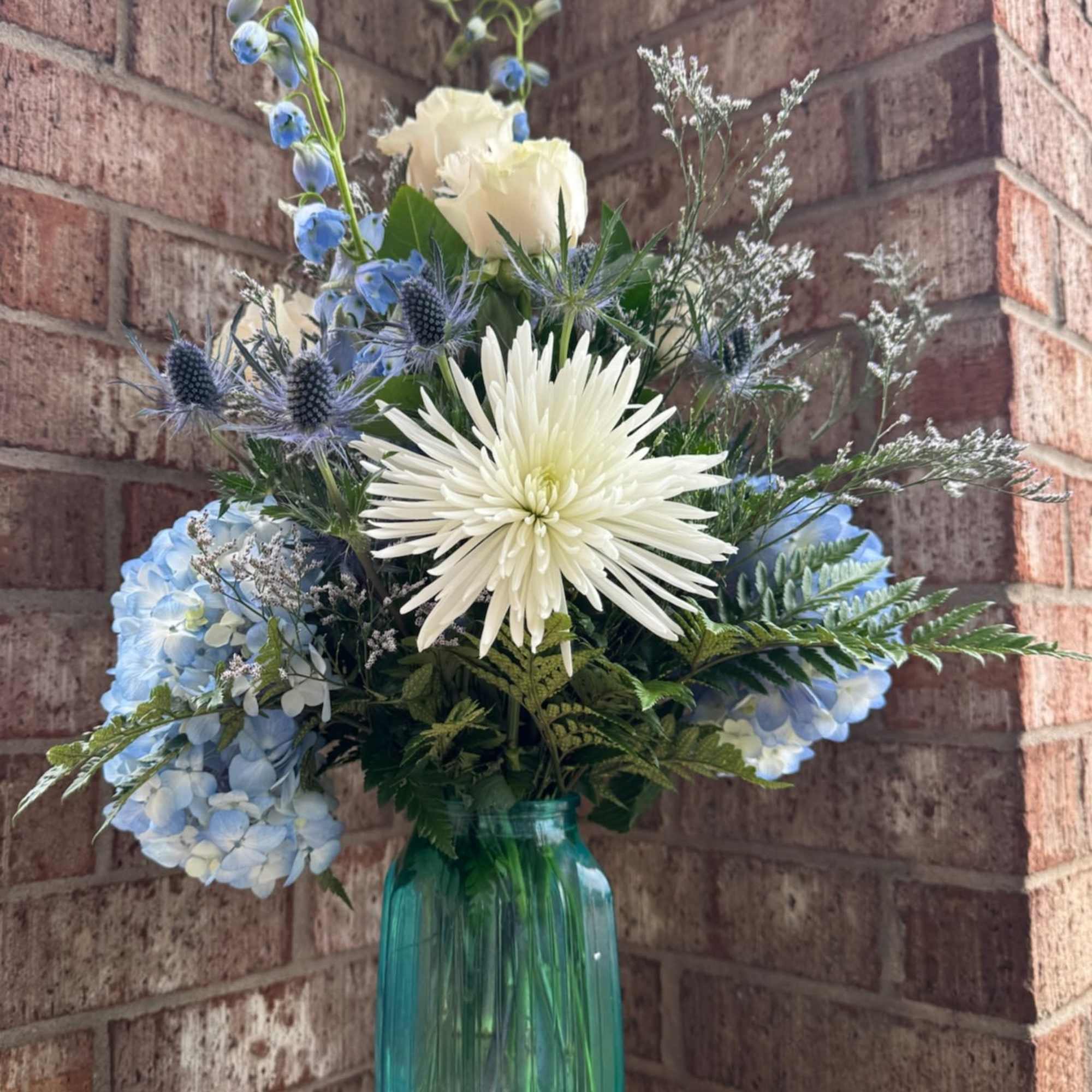 Blue and white floral arrangement in a tall teal glass vase