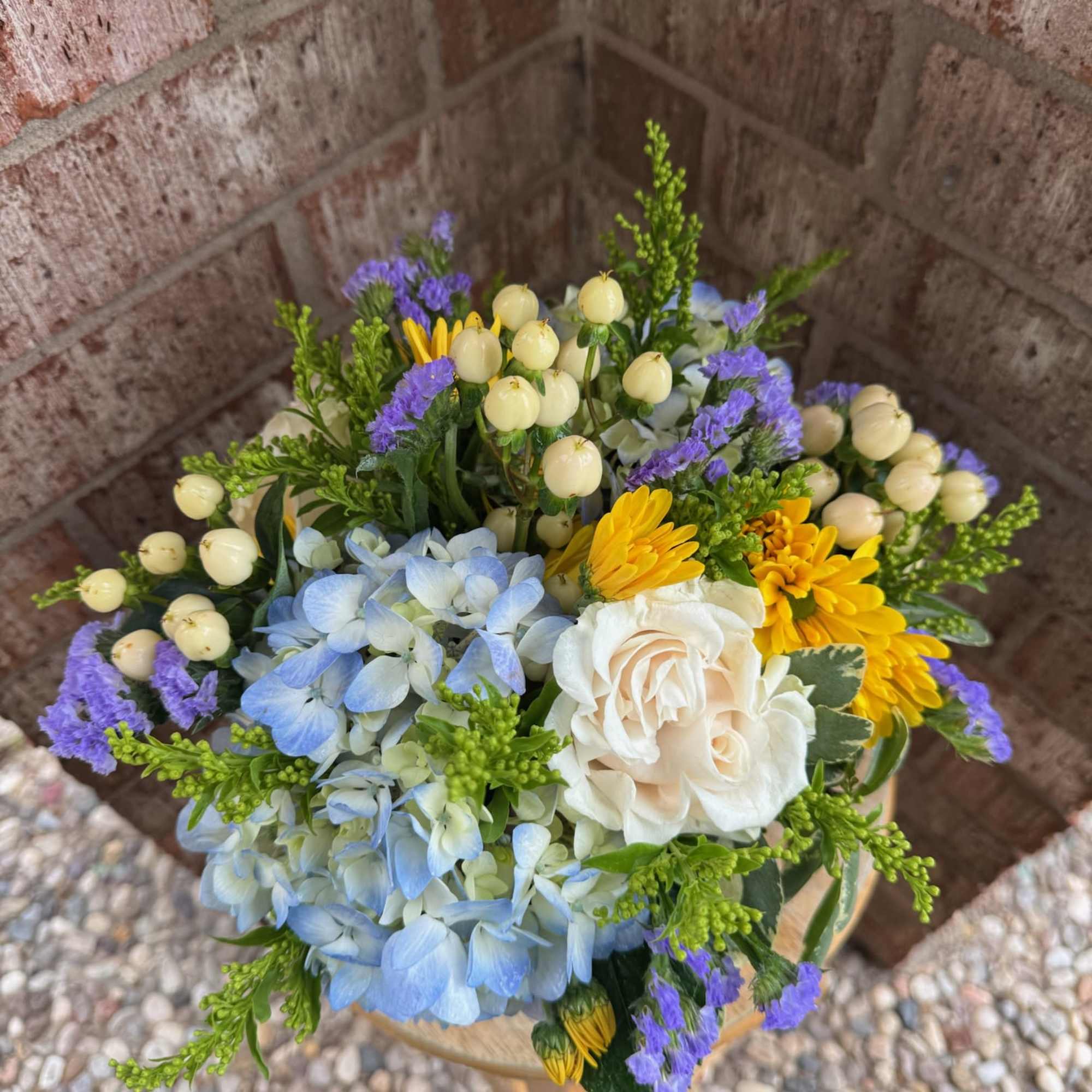 Bouquet of blue hydrangeas, white roses, yellow daisies, and purple filler flowers