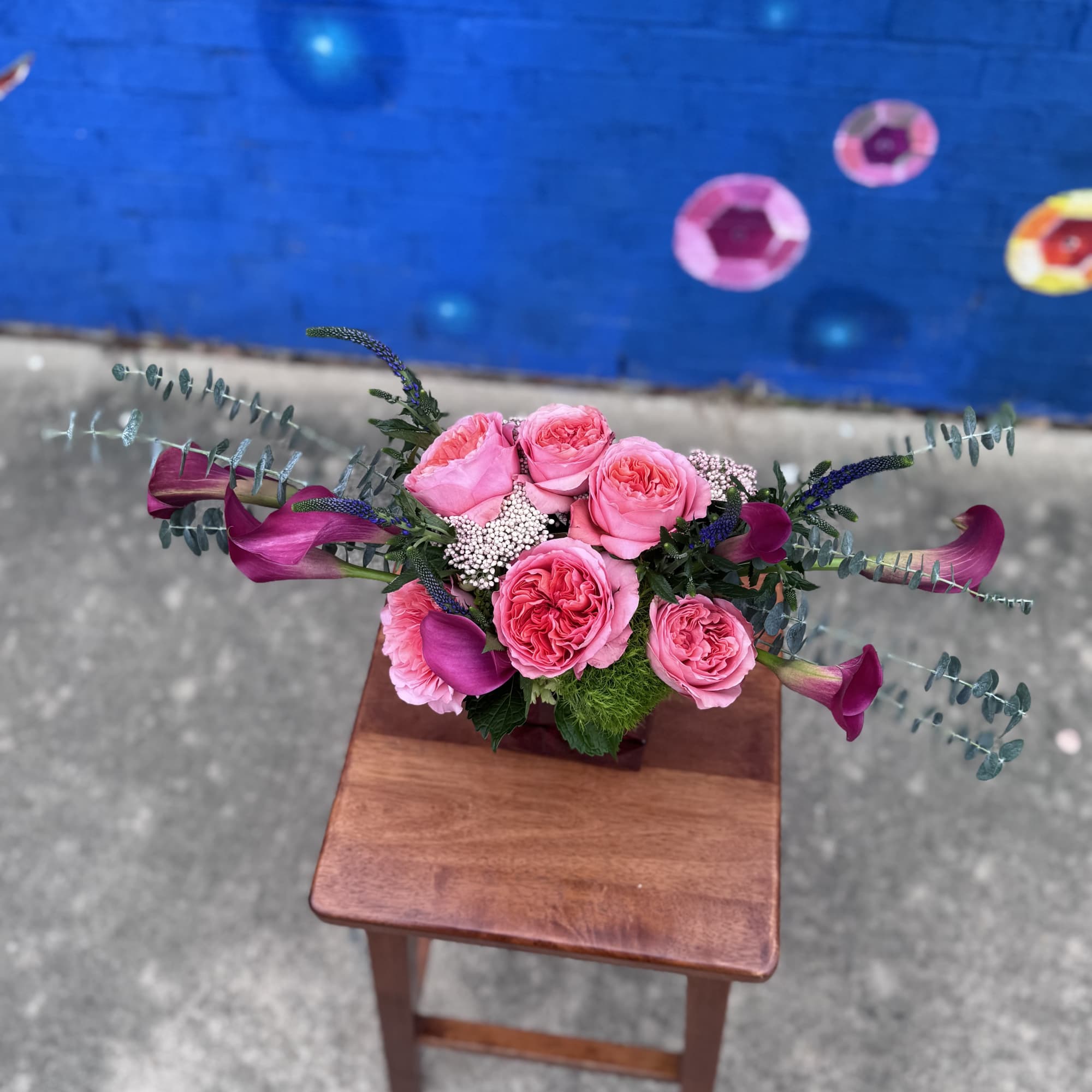 Pink rose arrangement with purple calla lilies in a low container