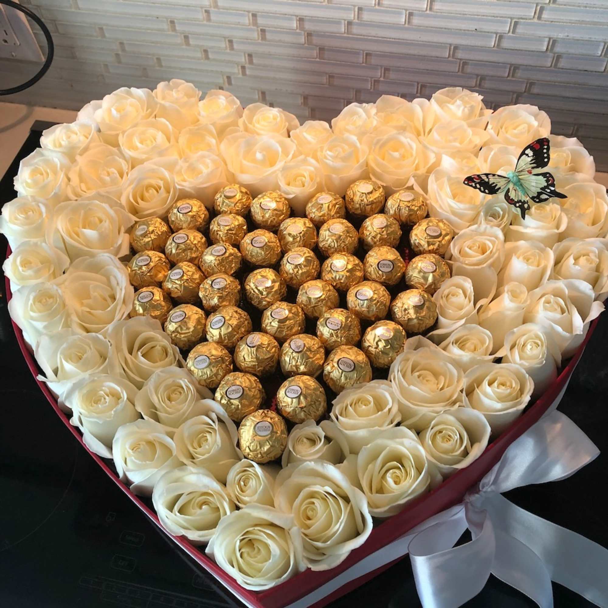 Heart-shaped box of white roses with gold-wrapped chocolates and a butterfly topper