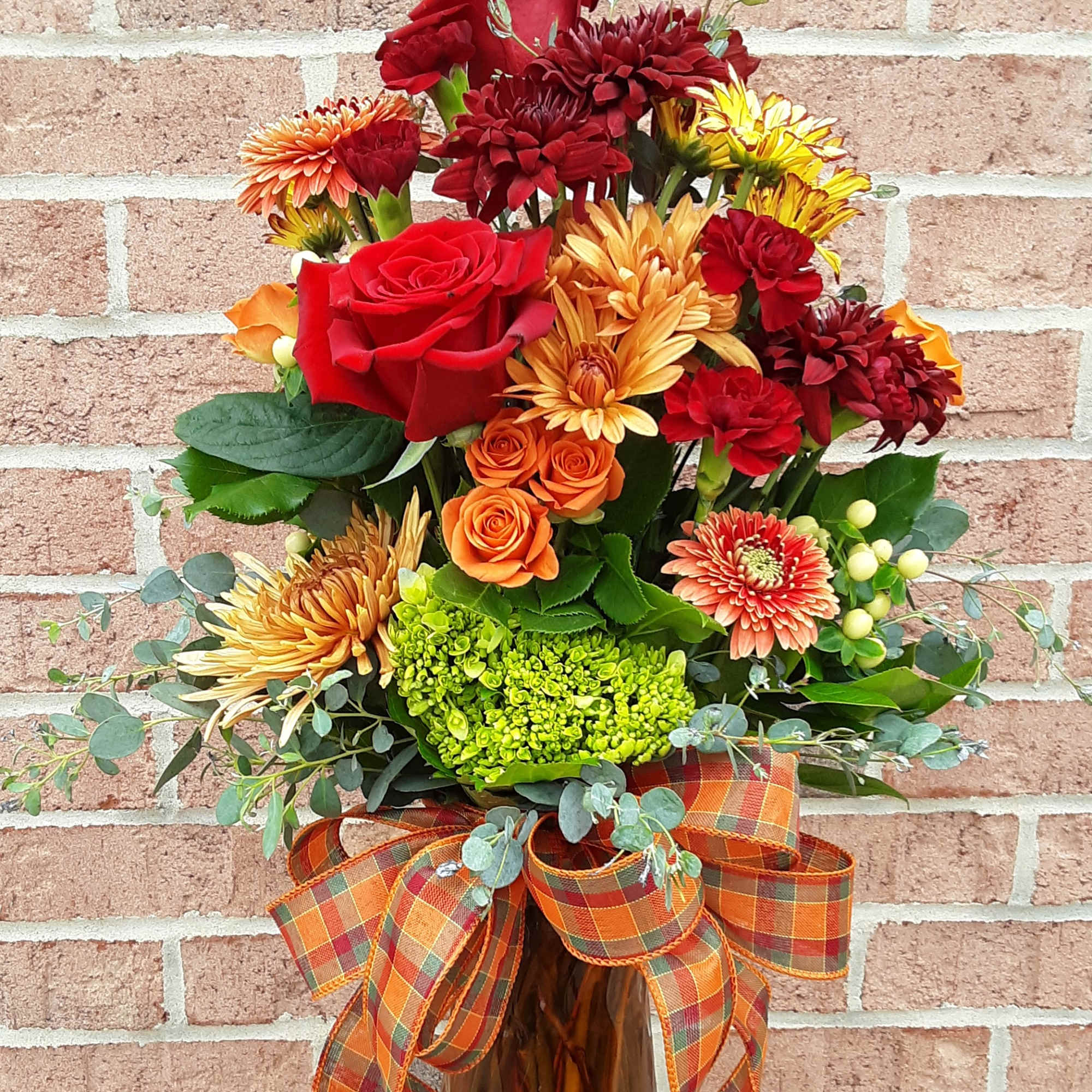 Autumn bouquet of red, orange, and yellow flowers in a glass vase with plaid ribbon