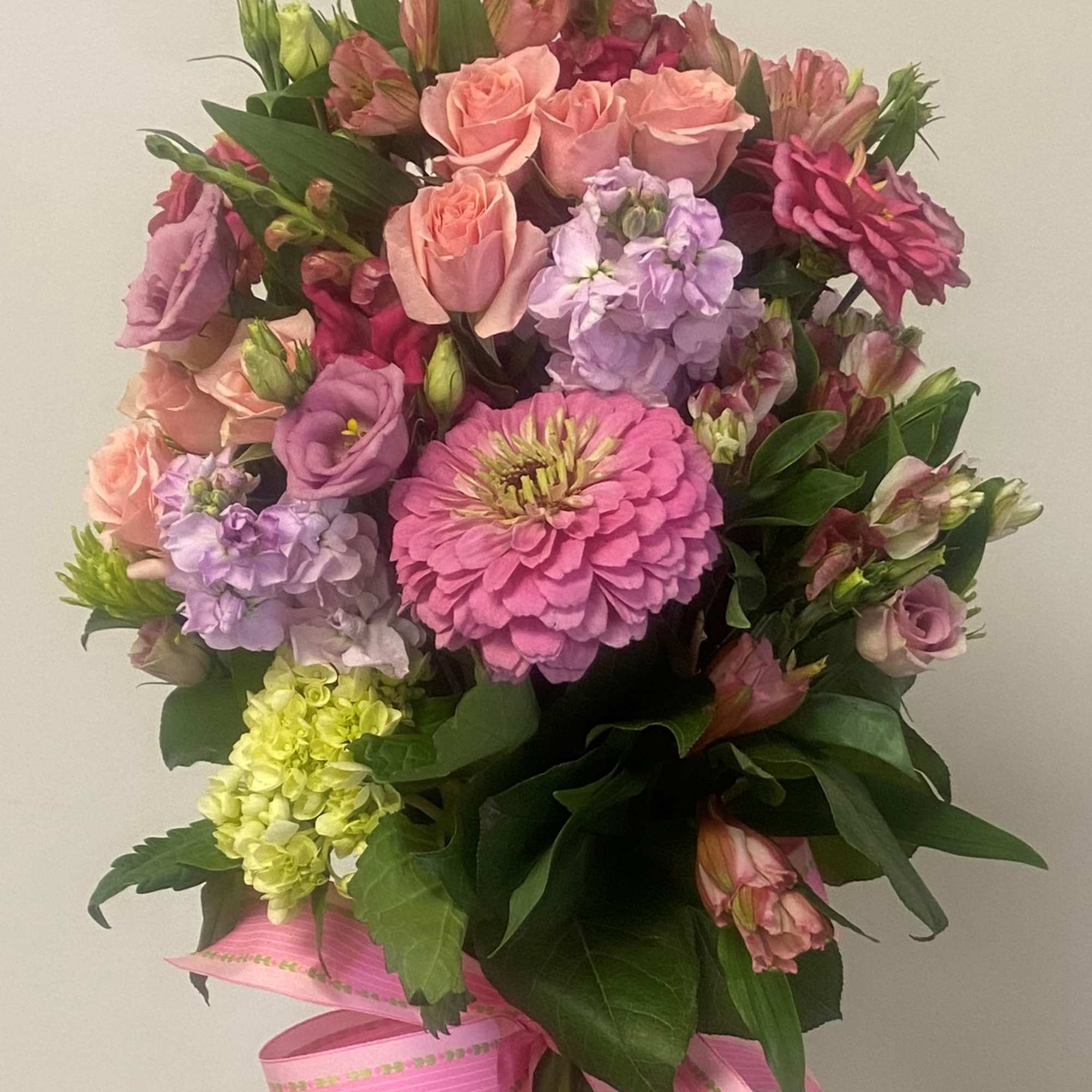 Pink and lavender mixed flower bouquet in a glass vase with a pink ribbon