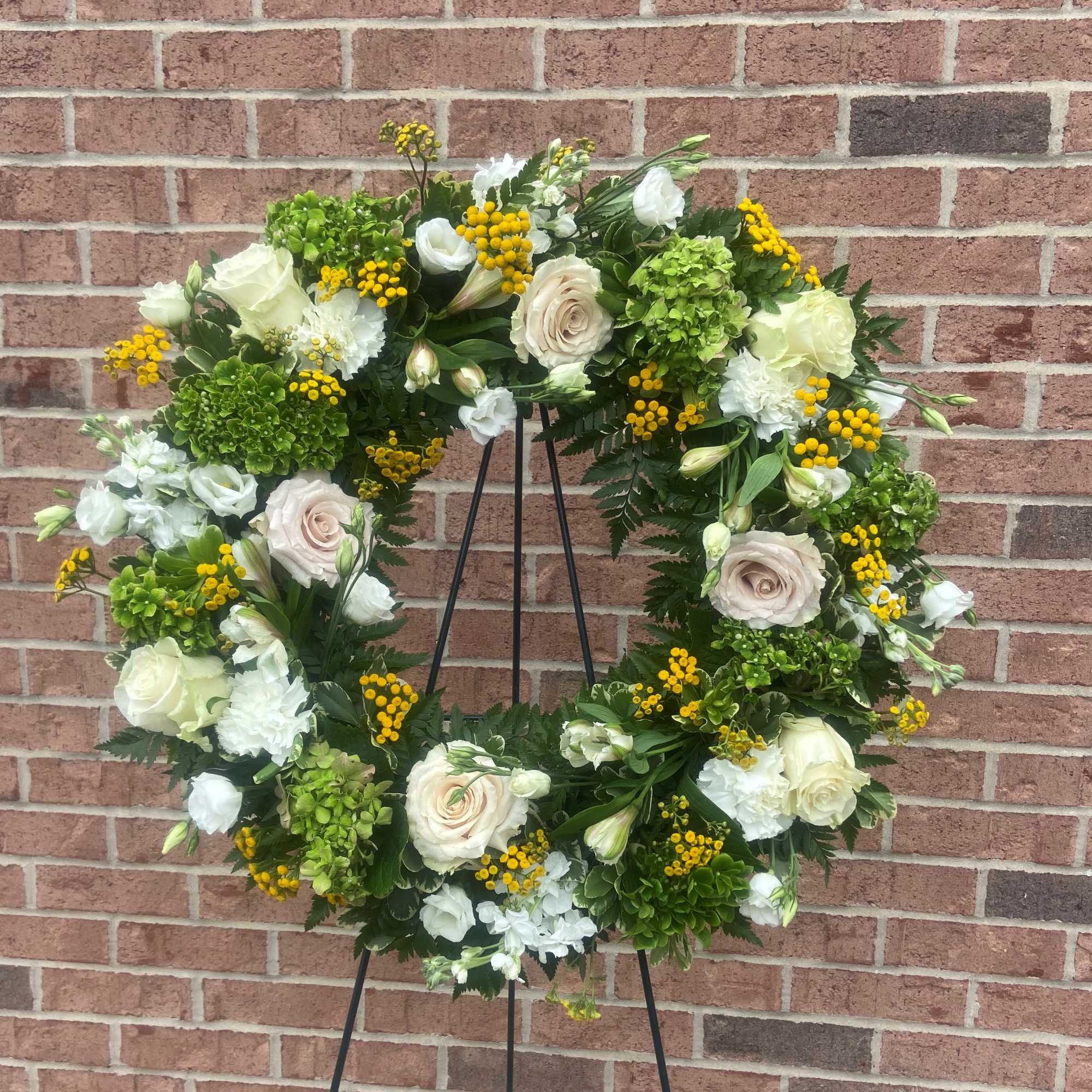 White and green floral wreath on a black stand