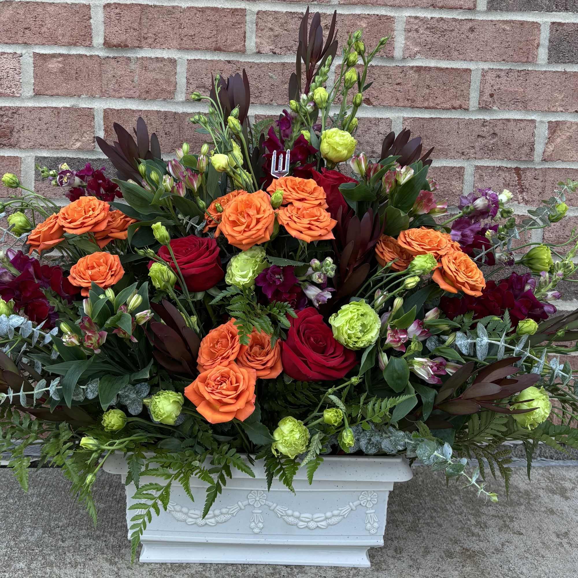 Large floral arrangement with orange and red roses in a white planter