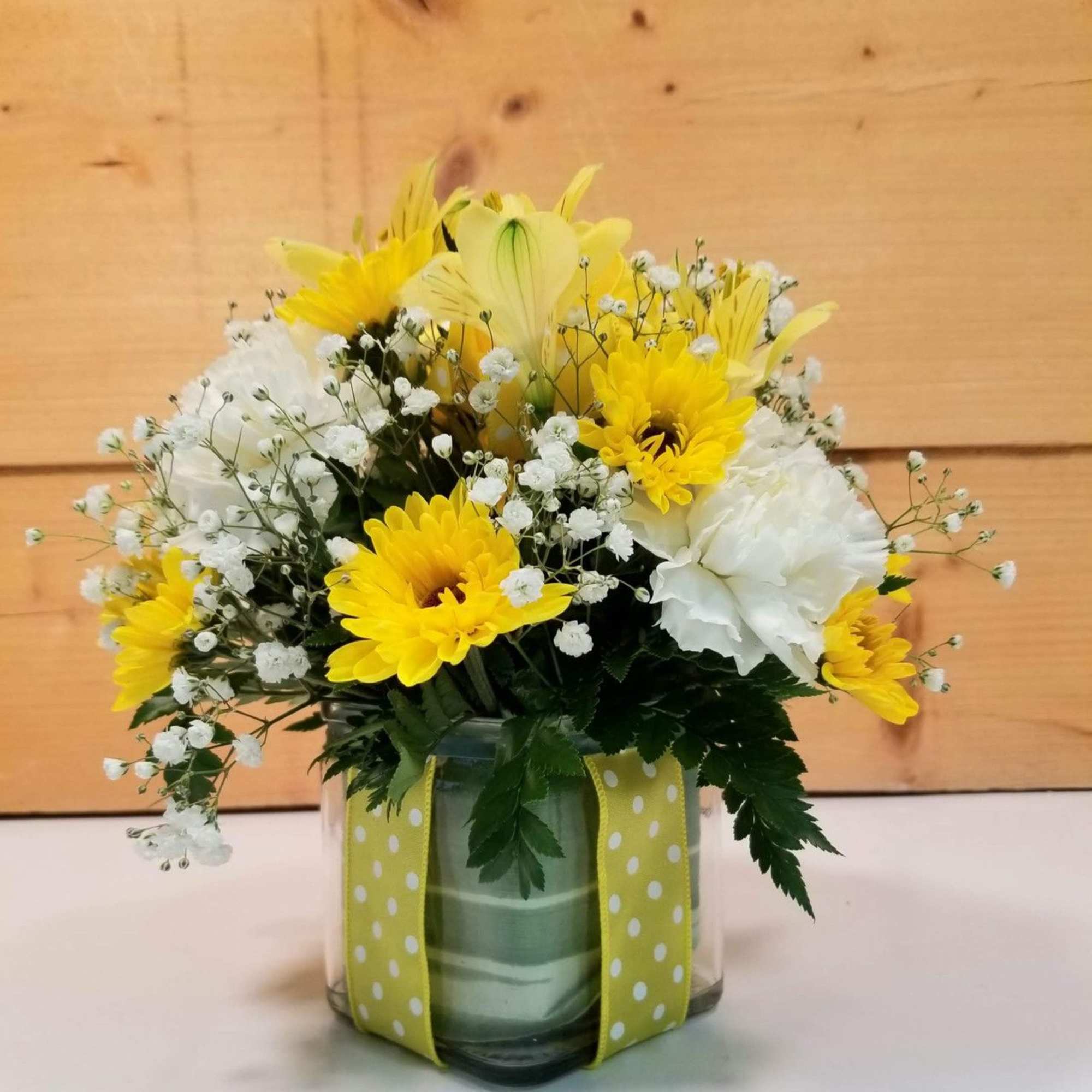 Yellow and white flower arrangement in a glass vase with polka-dot ribbon