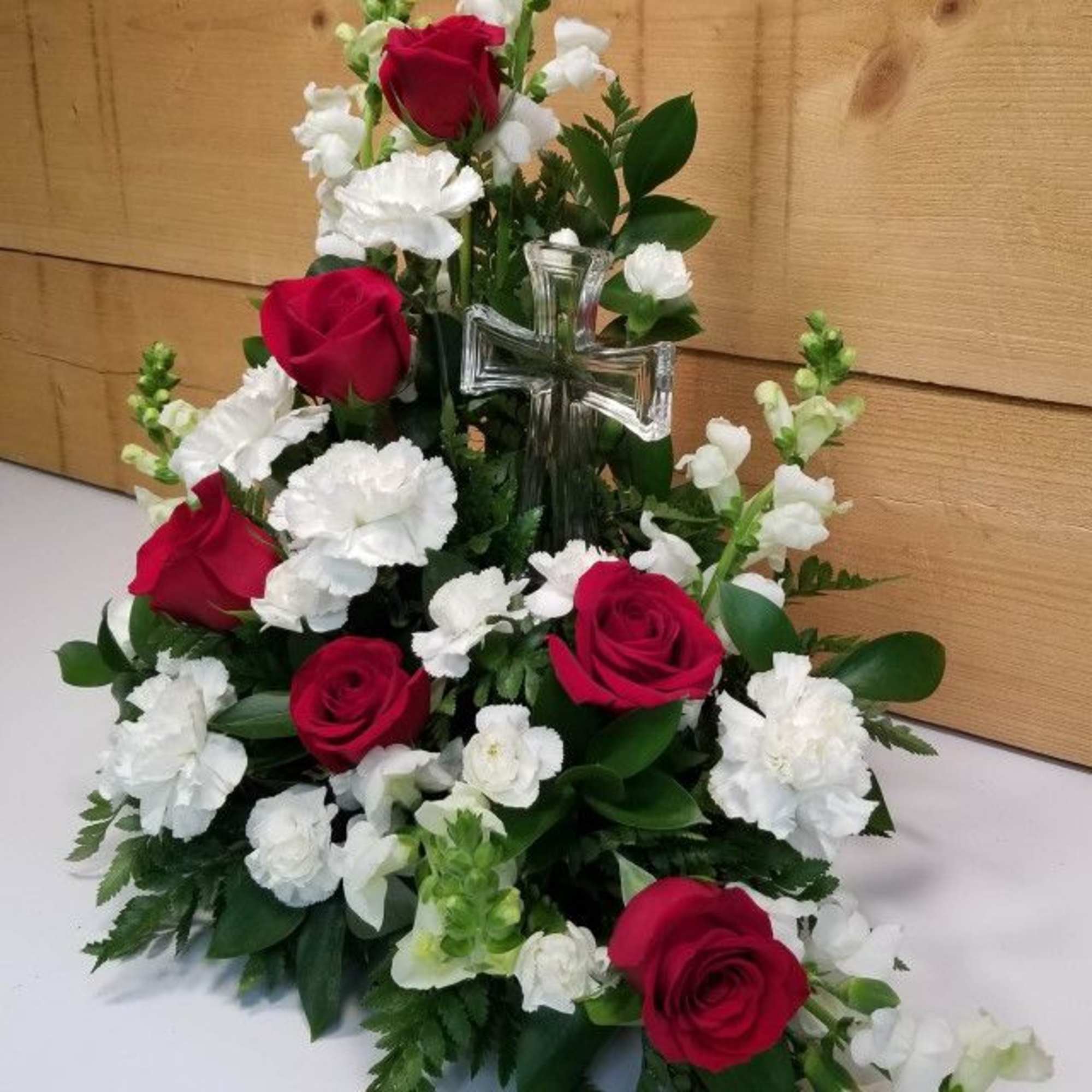 Red roses and white carnations arranged around a clear glass cross