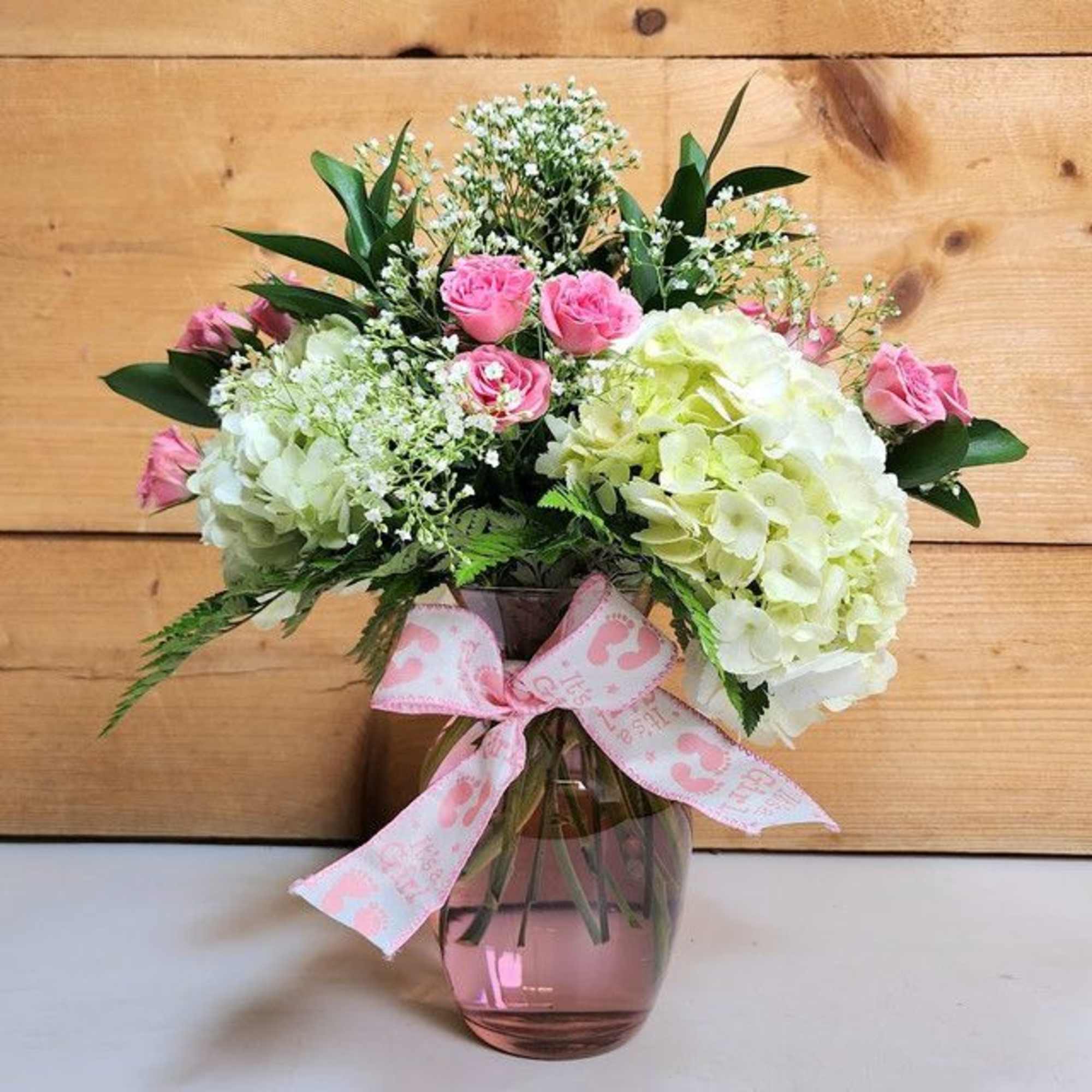 Pink roses and white hydrangeas in a glass vase with a pink ribbon