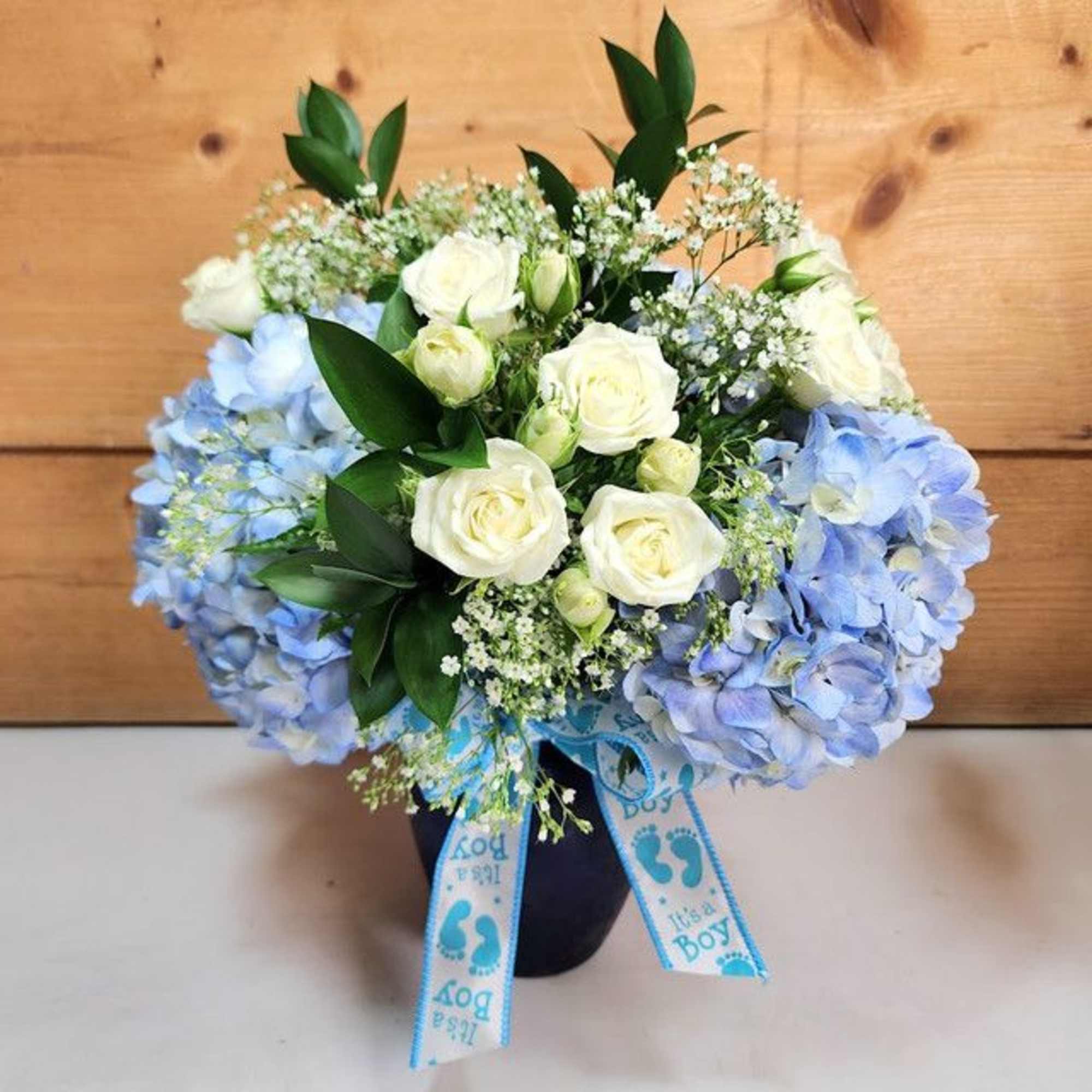 Blue hydrangeas and white roses in a vase with "It's a Boy" ribbons