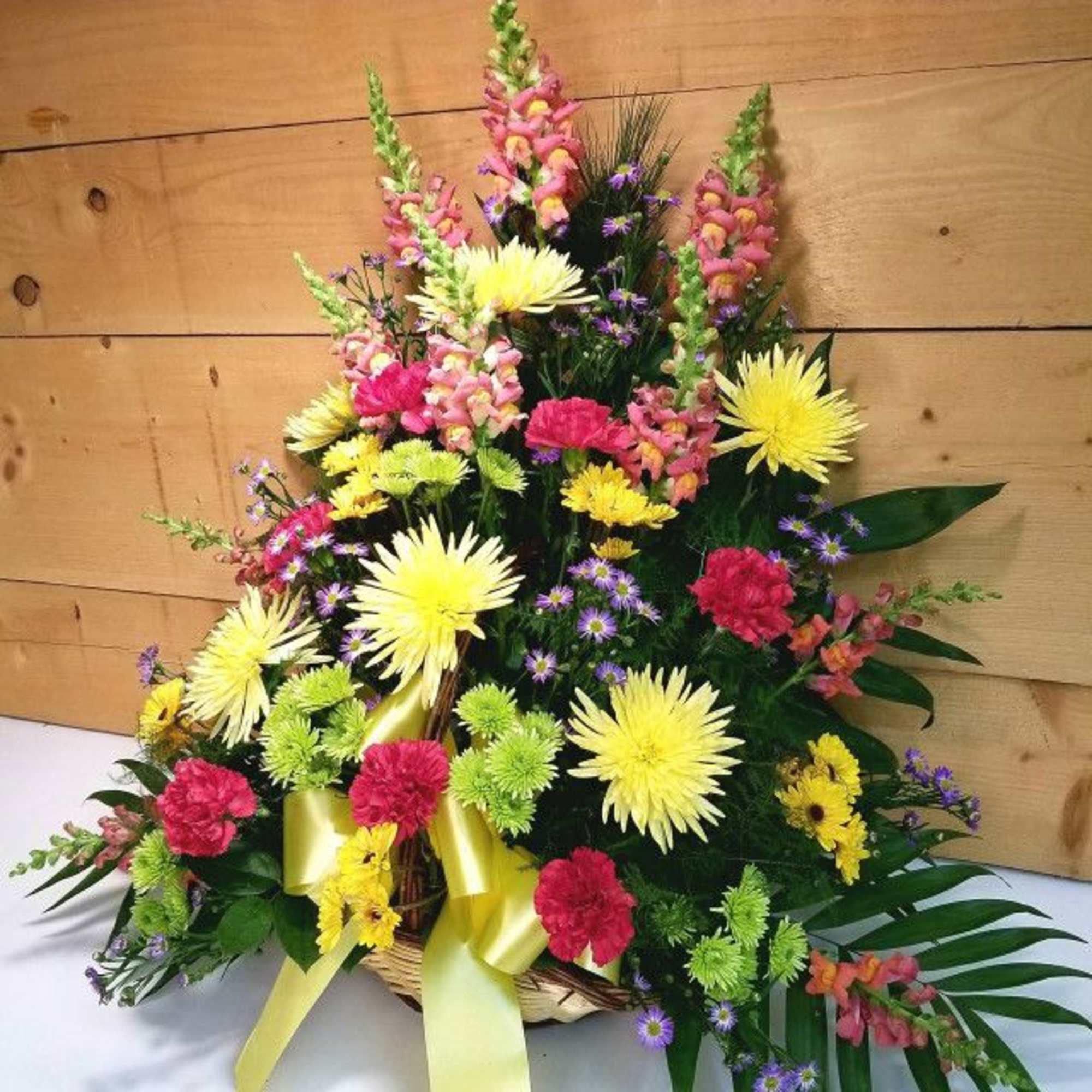 Basket arrangement of yellow, pink, and purple flowers with a yellow ribbon