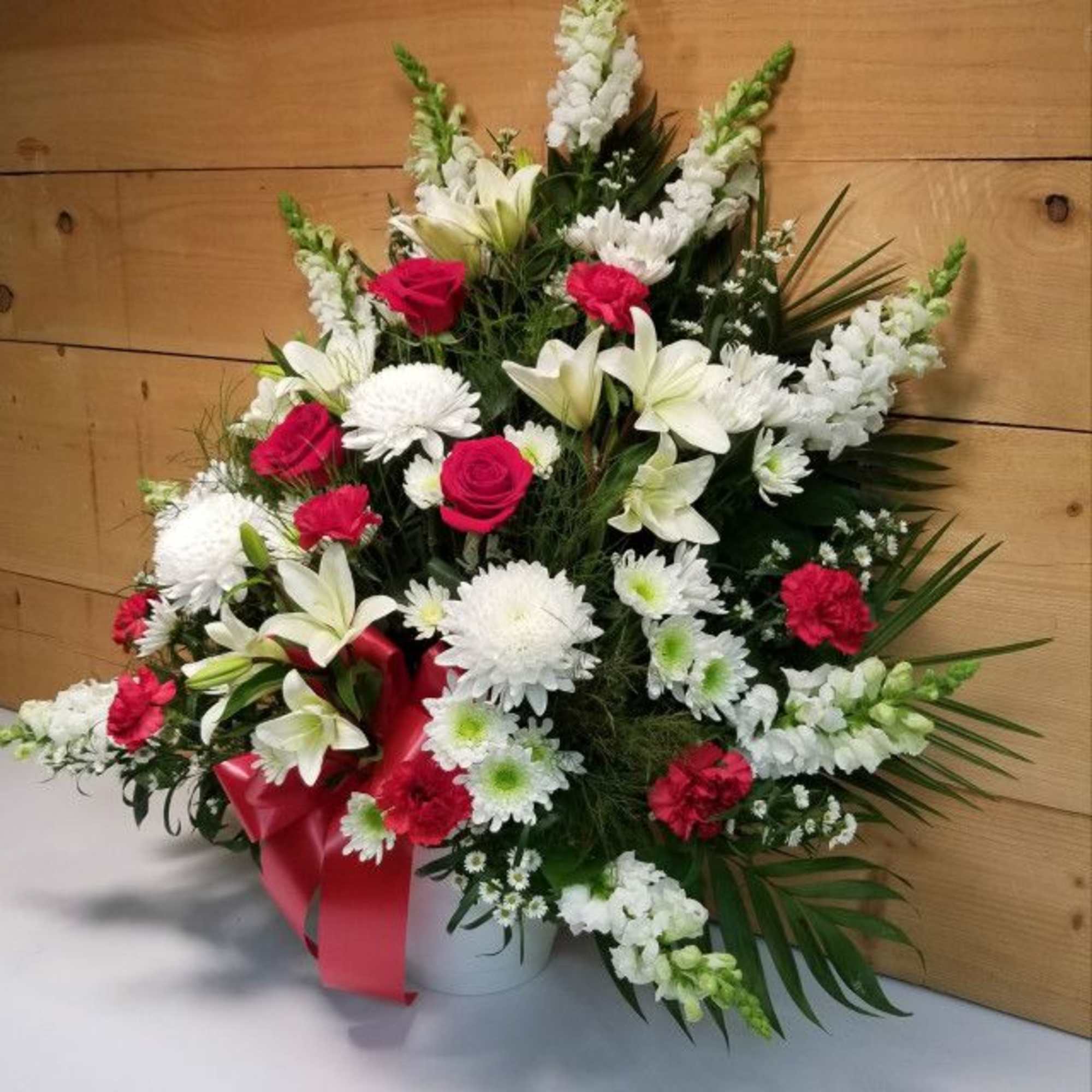 White and red floral arrangement in a white container with a red ribbon
