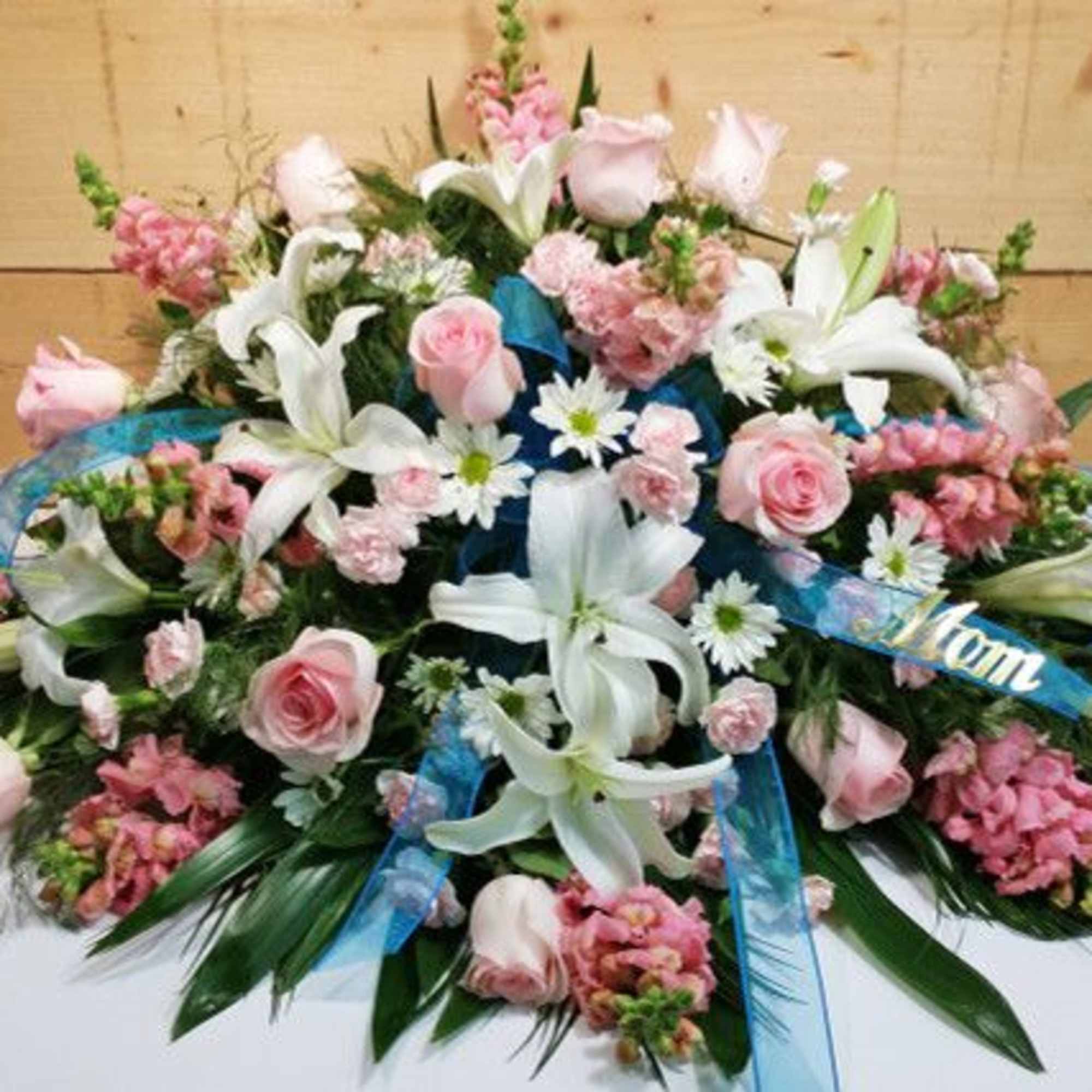 Pink roses and white lilies arranged with blue ribbons on a flat spray.