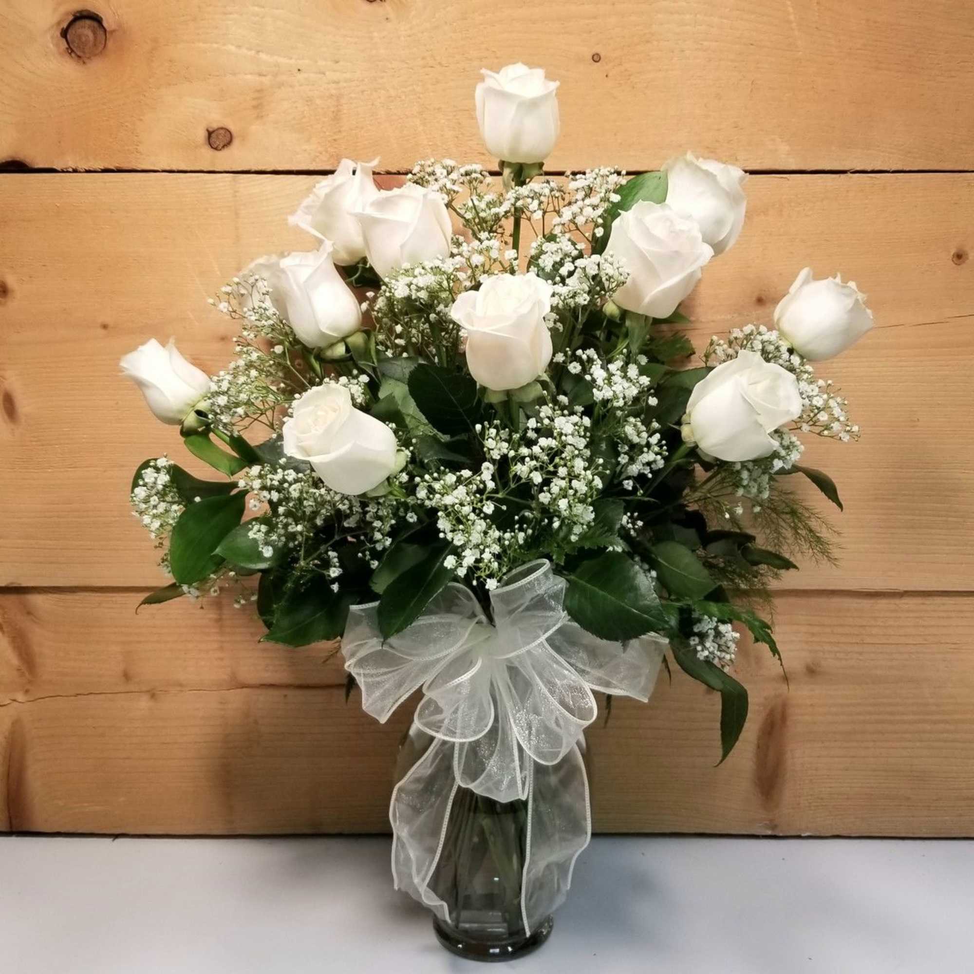 White roses arranged in a glass vase with a sheer white bow