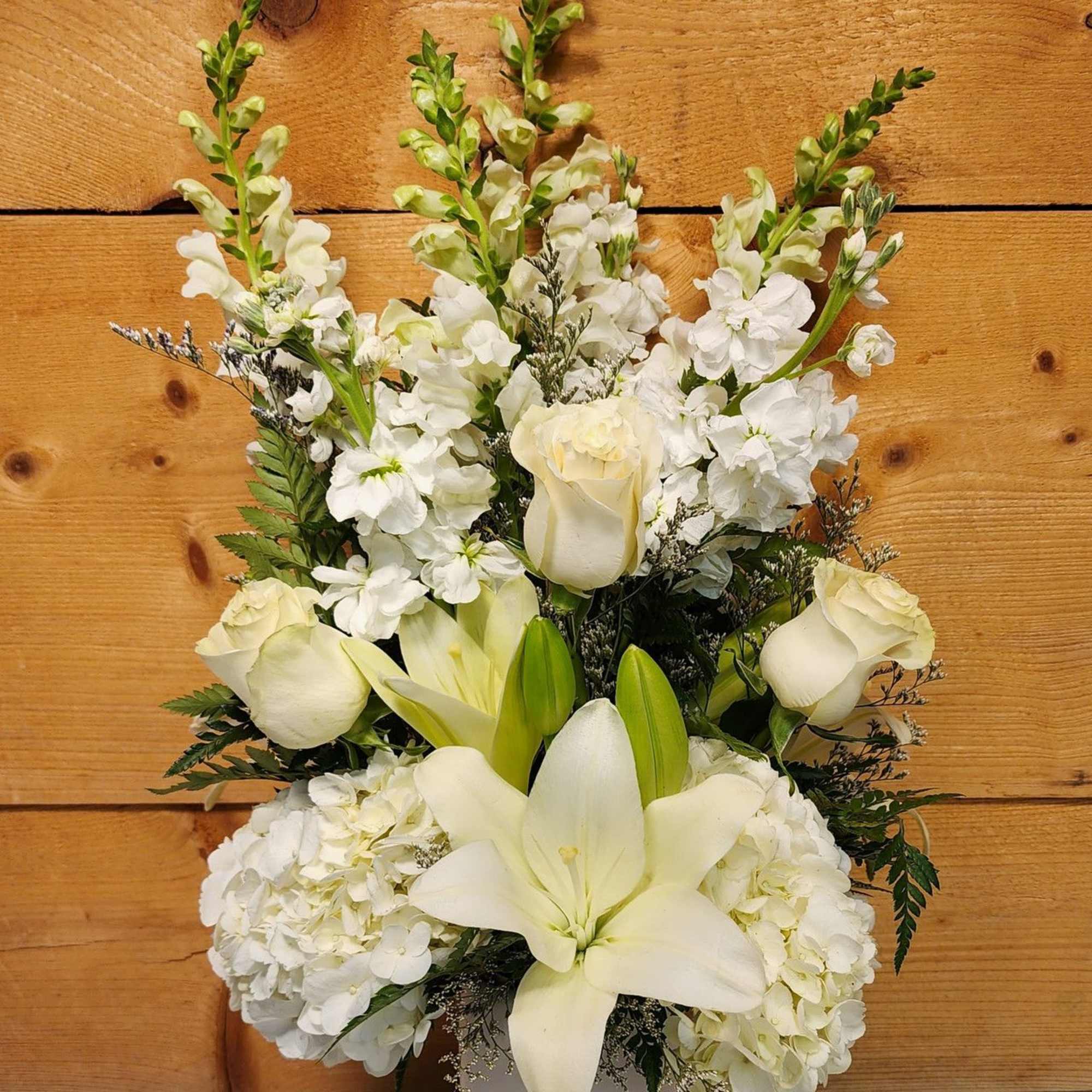 White floral arrangement with roses, lilies, and tall snapdragons