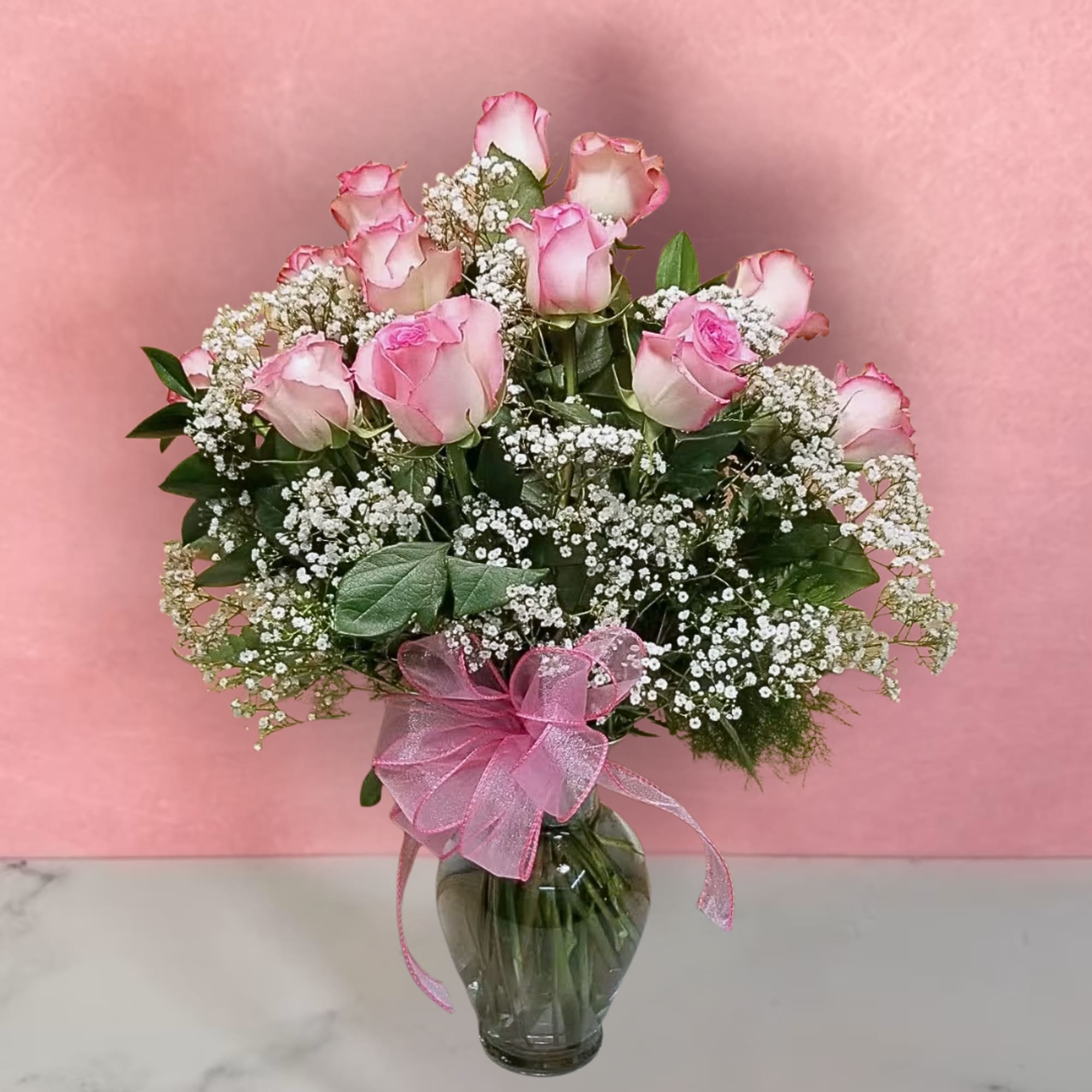 Pink roses arranged in a glass vase with baby's breath and a pink ribbon
