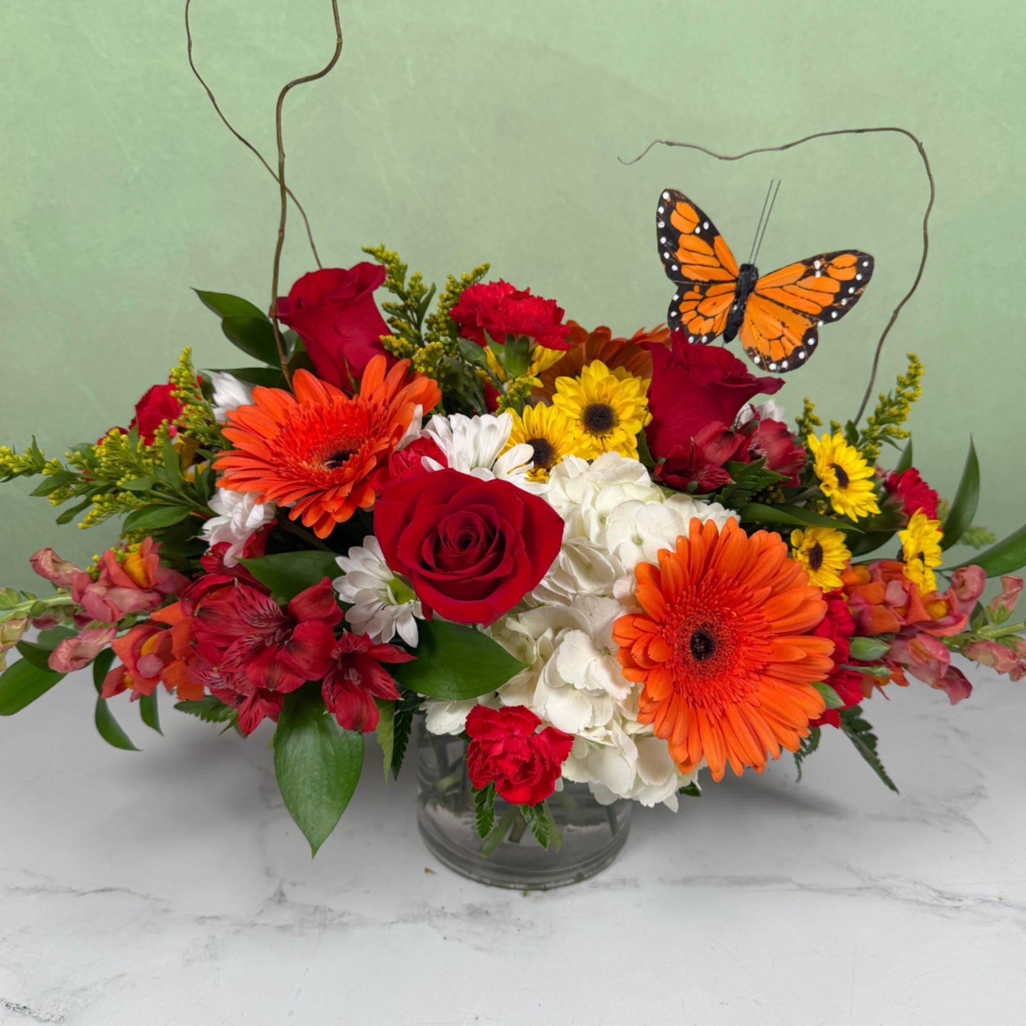 Bright mixed bouquet in a glass vase with a butterfly accent