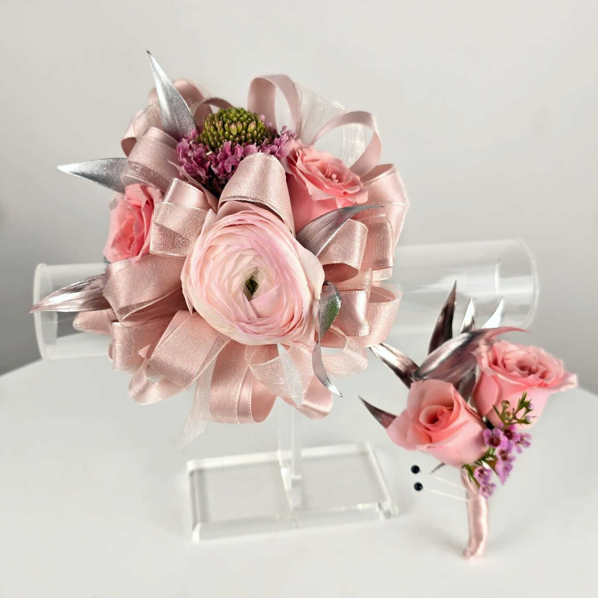 Pink floral bouquet and matching boutonniere with ribbon on a clear stand