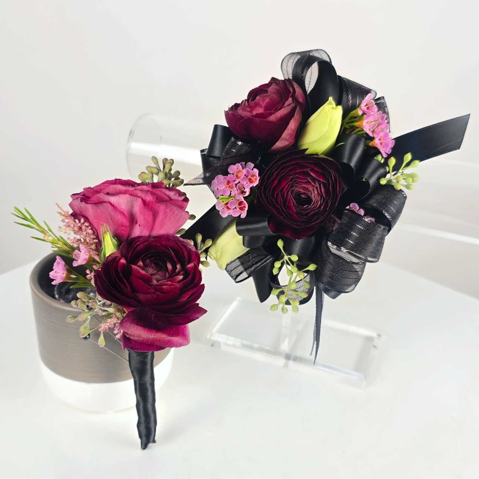 Two burgundy and pink floral boutonnieres with black ribbon accents