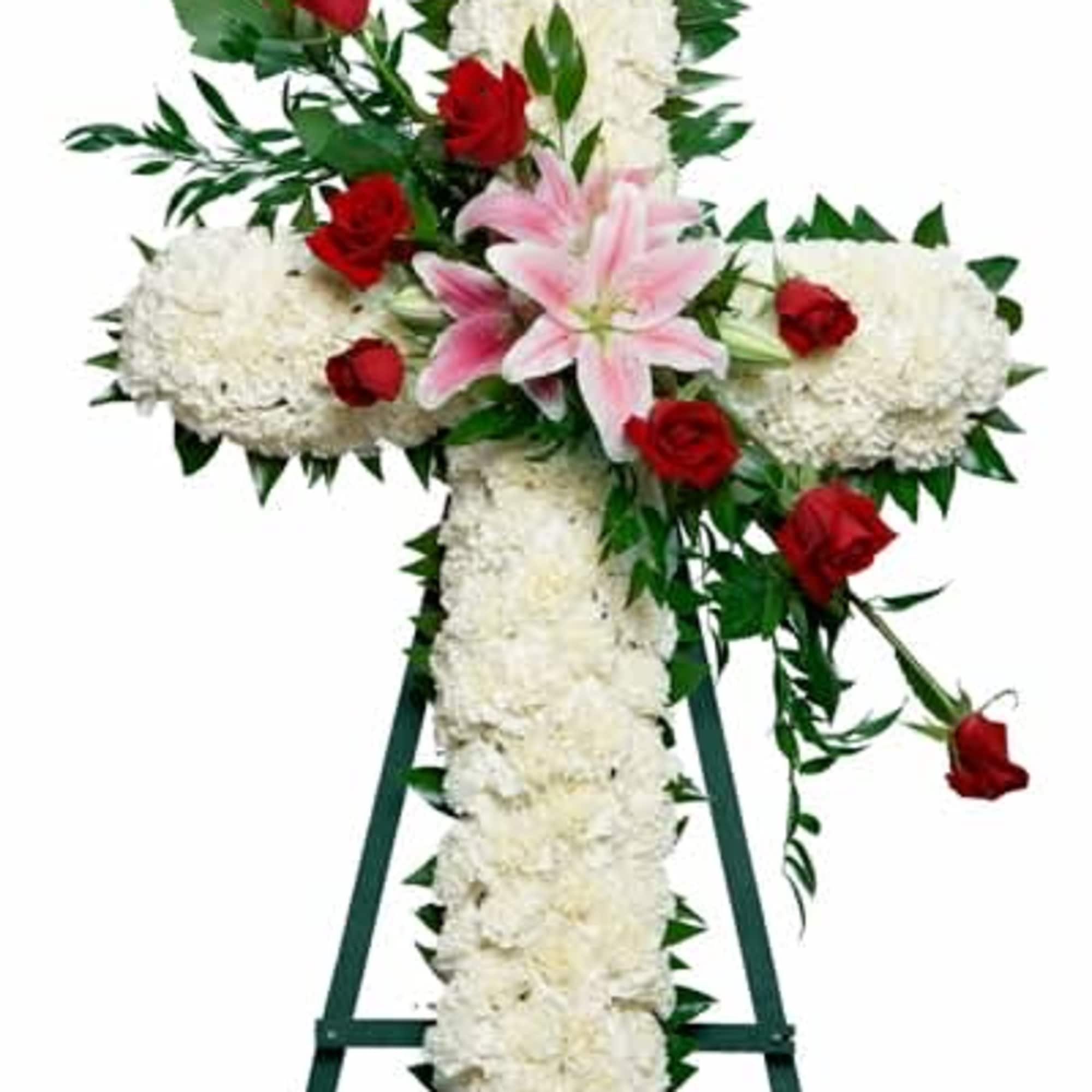 White floral cross on an easel with red roses and a pink lily