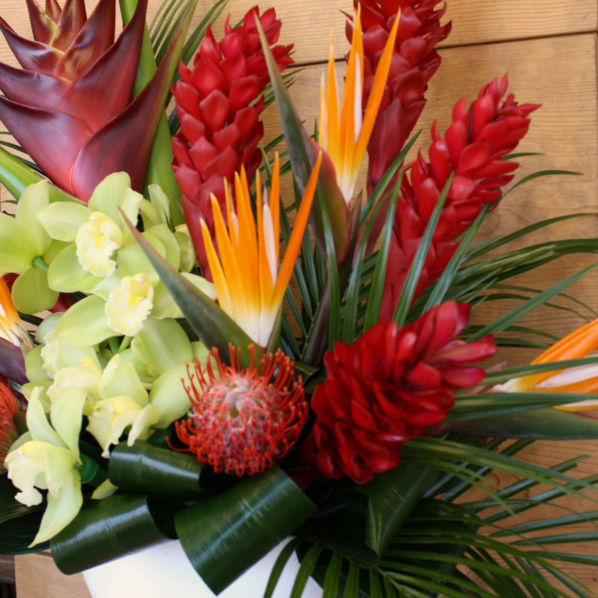 Tropical bouquet with red ginger, bird of paradise, and pale green orchids in a white vase