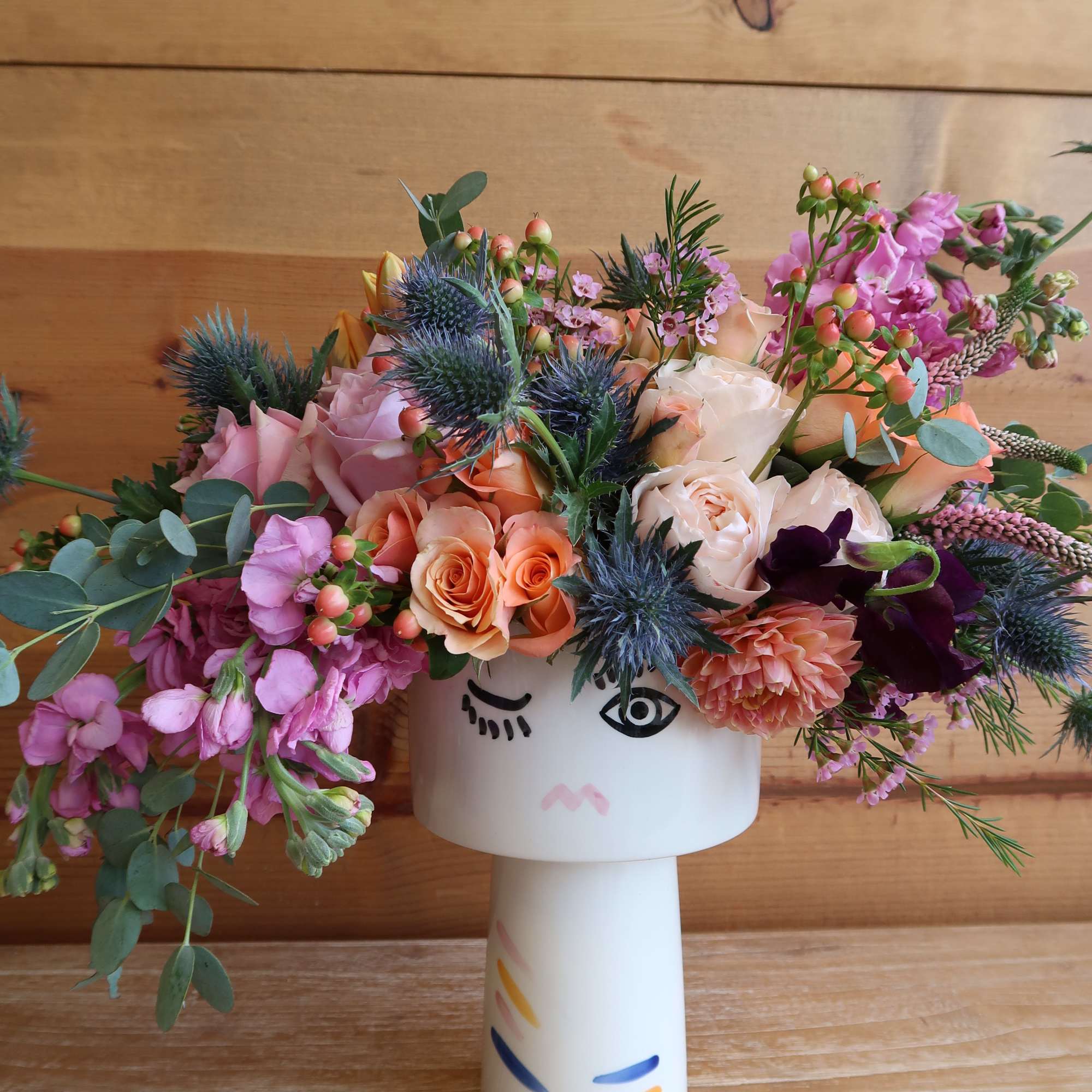 Mixed bouquet of pink, peach, and purple flowers in a white vase
