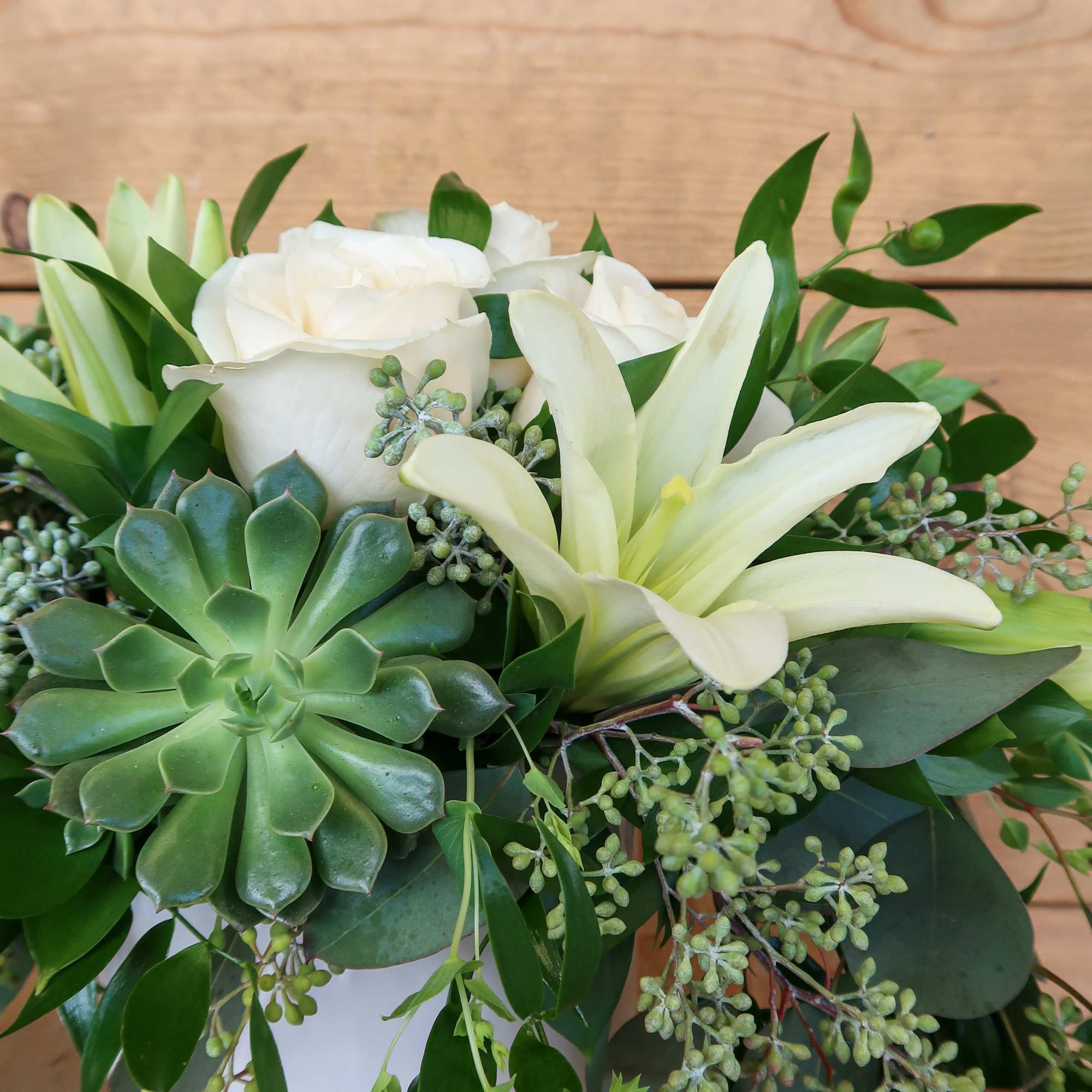 White roses and lilies in a white vase with succulents