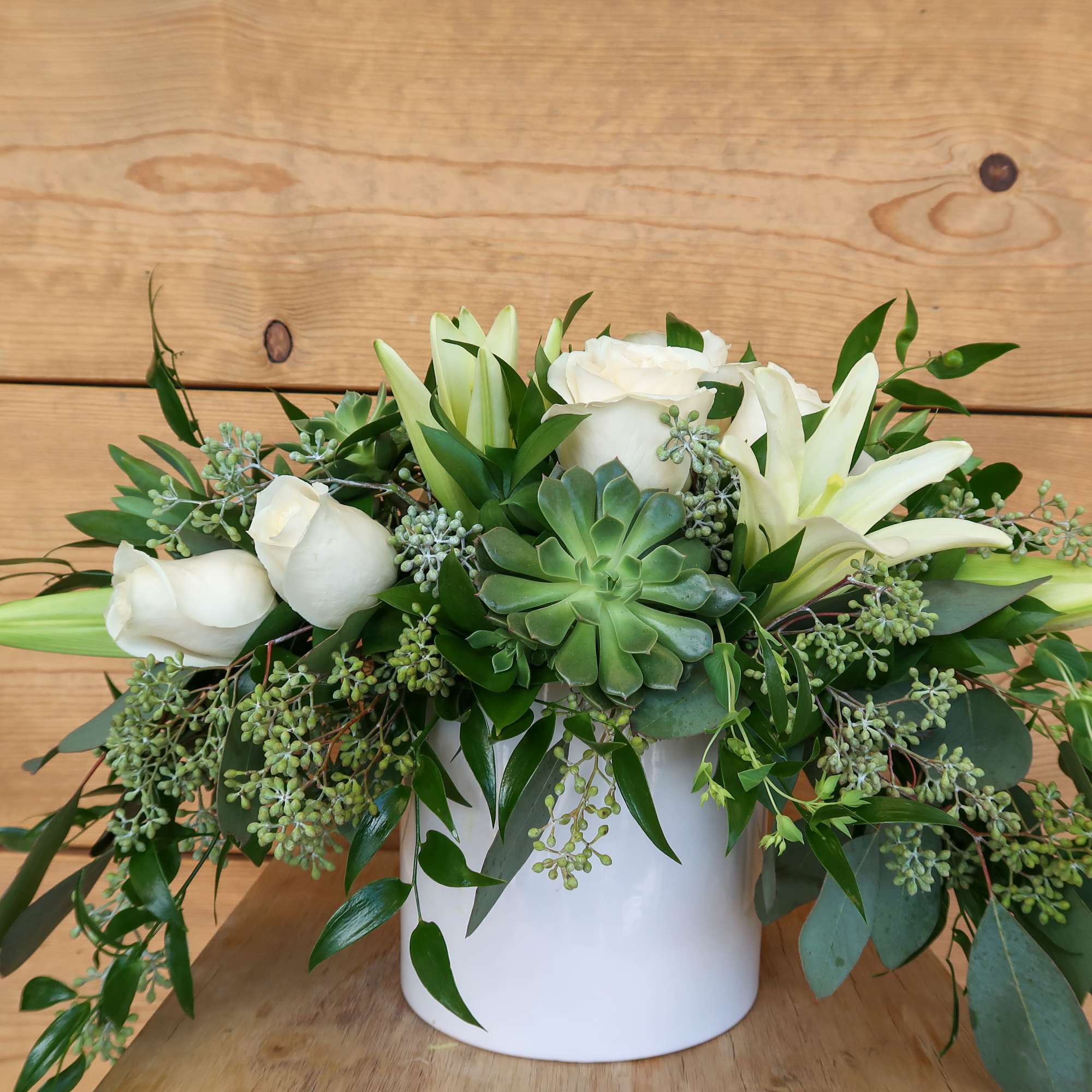 White roses and lilies arranged with succulents in a white container
