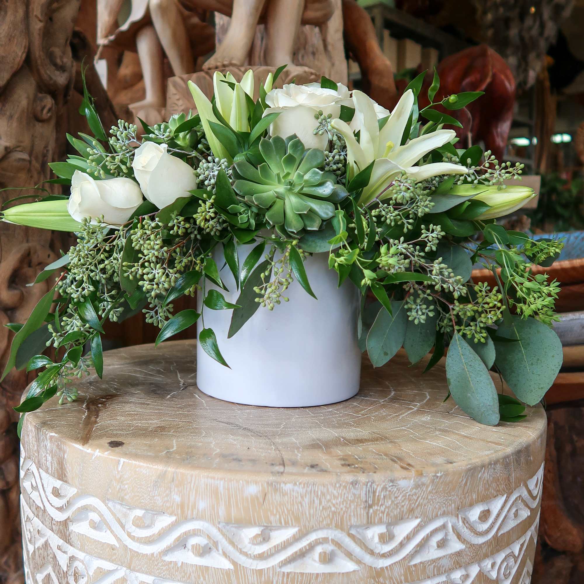 White roses and lilies arranged with succulents in a white vase